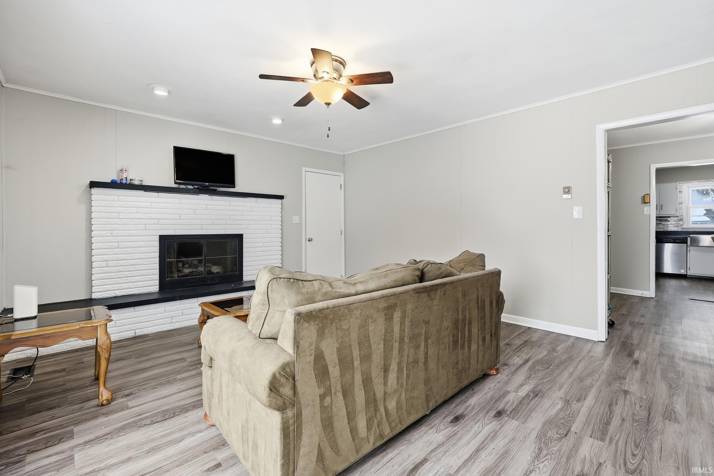 Living room featuring light wood-style flooring, a fireplace, ceiling fan, and ornamental molding