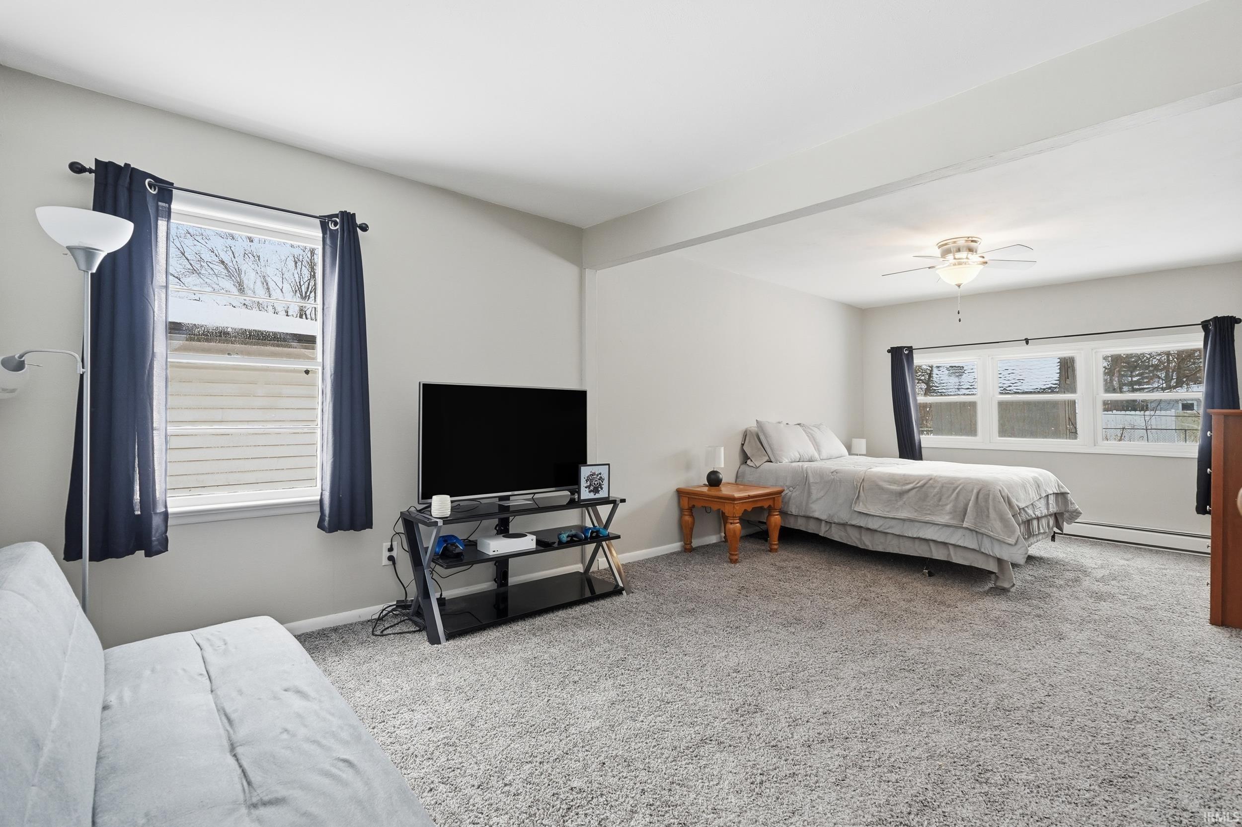 Bedroom featuring carpet floors, multiple windows, and a baseboard heating unit