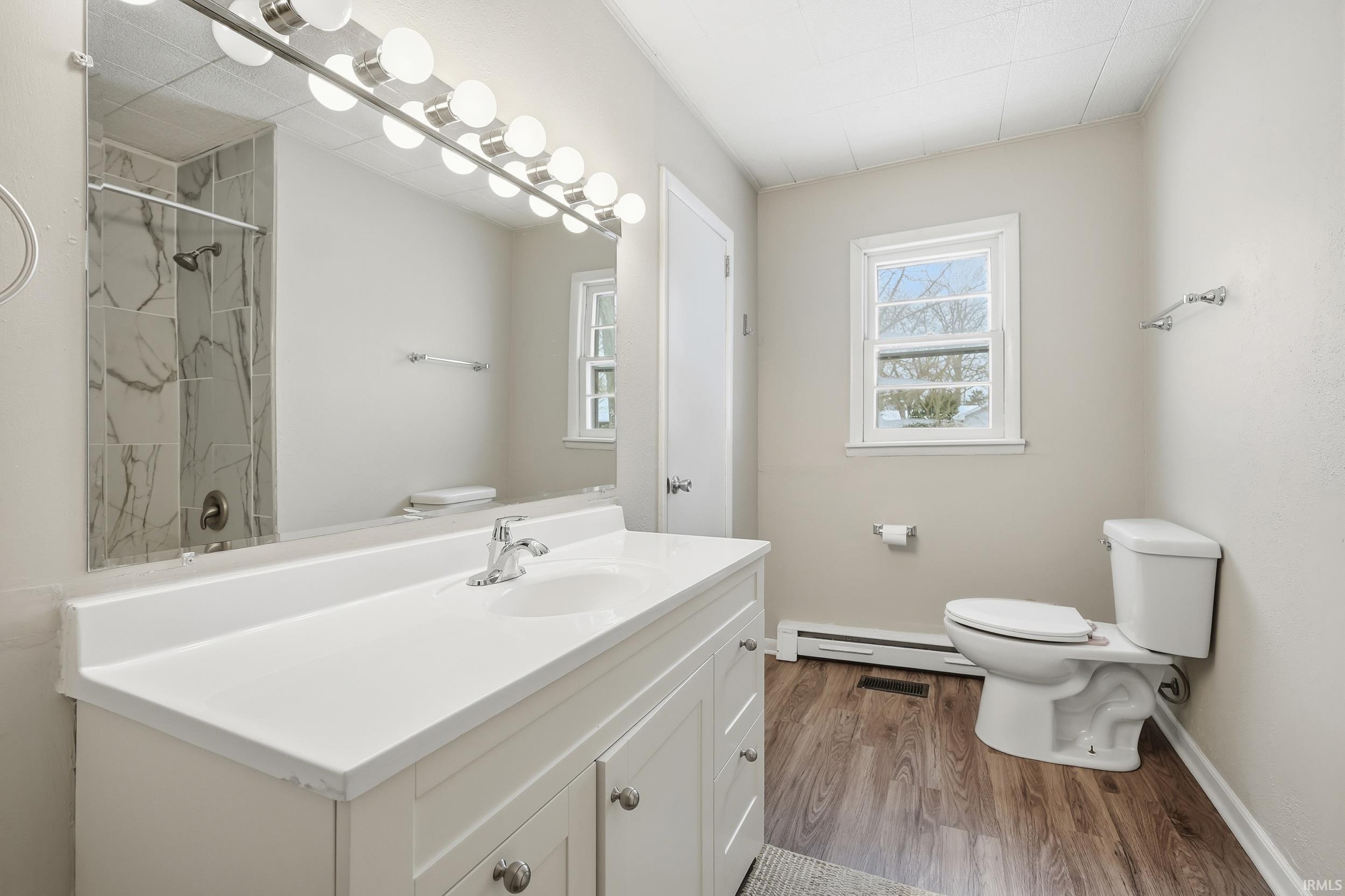 Bathroom with vanity, dark wood-type flooring, a tile shower, and a baseboard heating unit