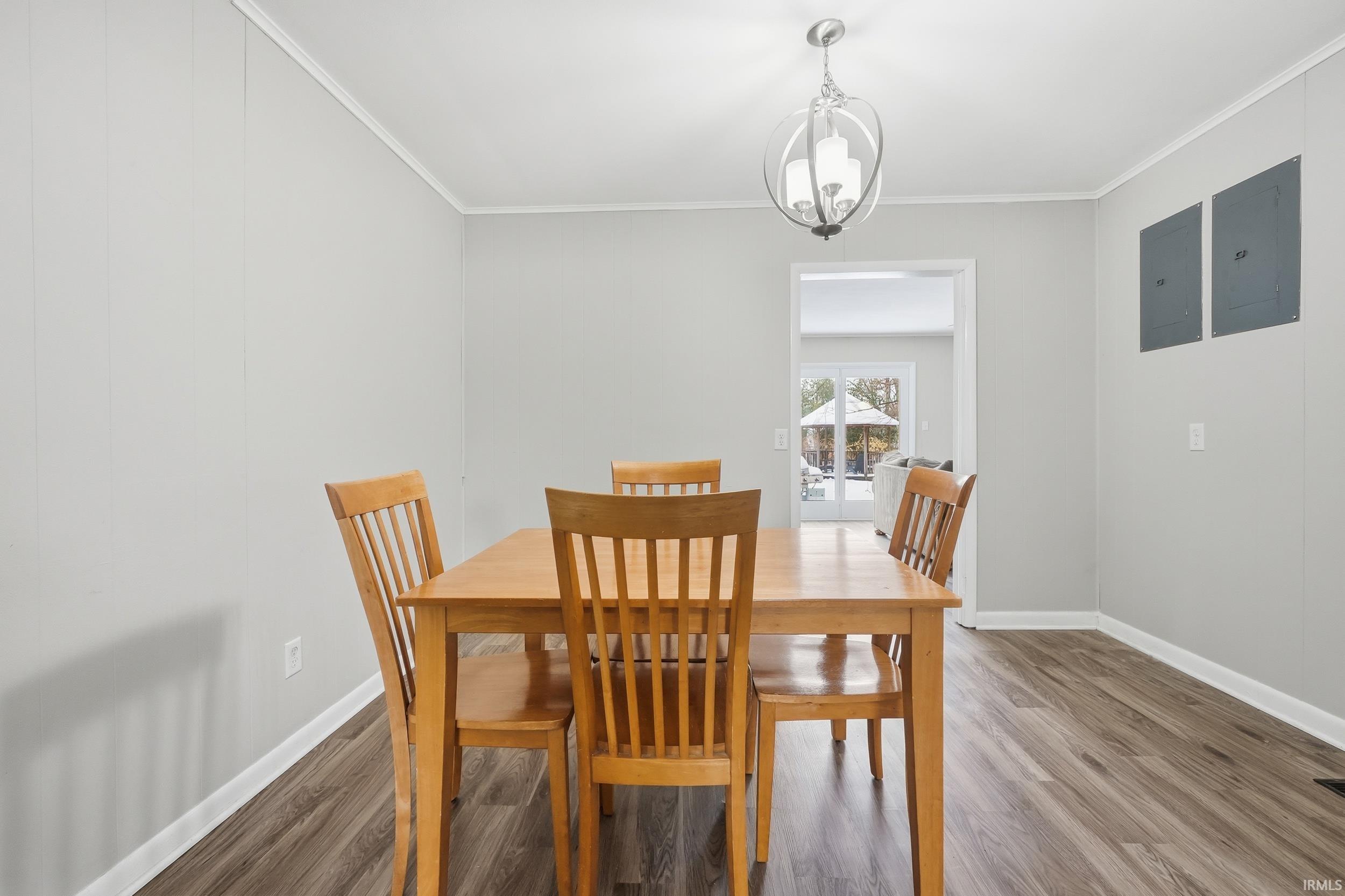 Dining room with electric panel, wood finished floors, crown molding, and suspended lighting
