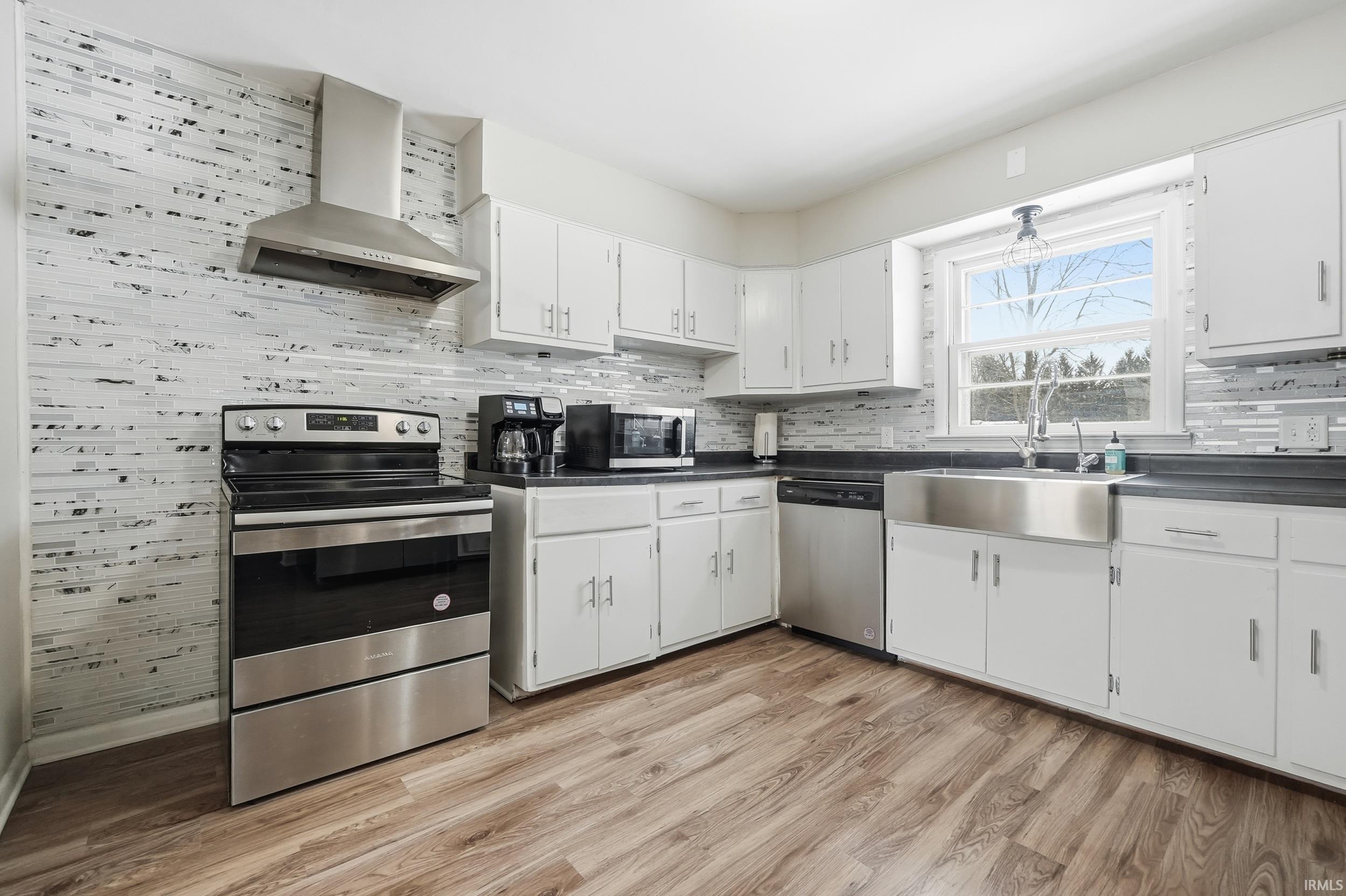 Kitchen with stainless steel appliances, white cabinetry, dark countertops, light wood-style flooring, and backsplash