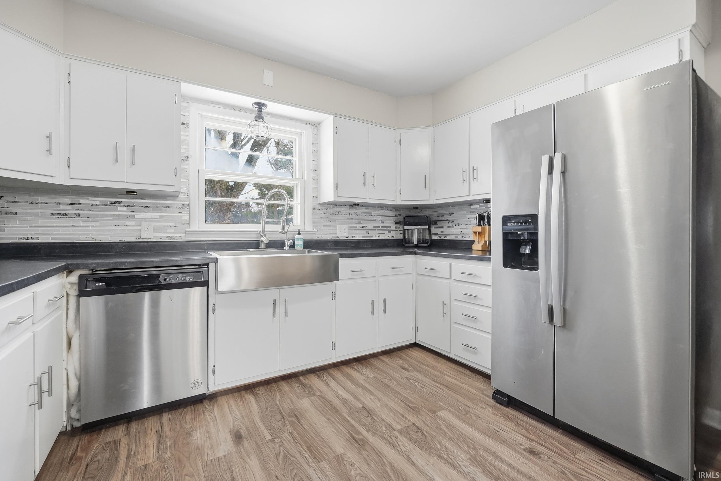 Kitchen featuring stainless steel appliances, white cabinetry, dark countertops, and light wood finished floors