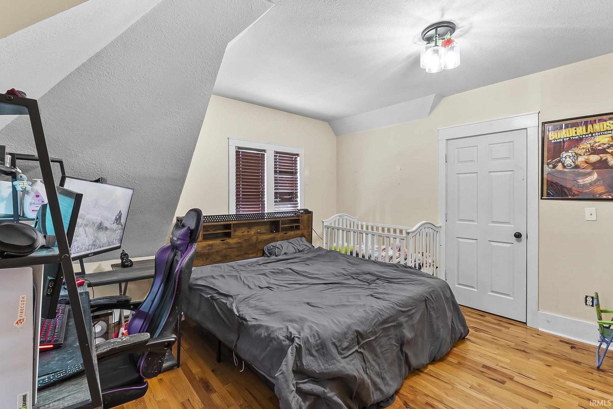 Bedroom featuring a textured wall, light wood finished floors, and lofted ceiling