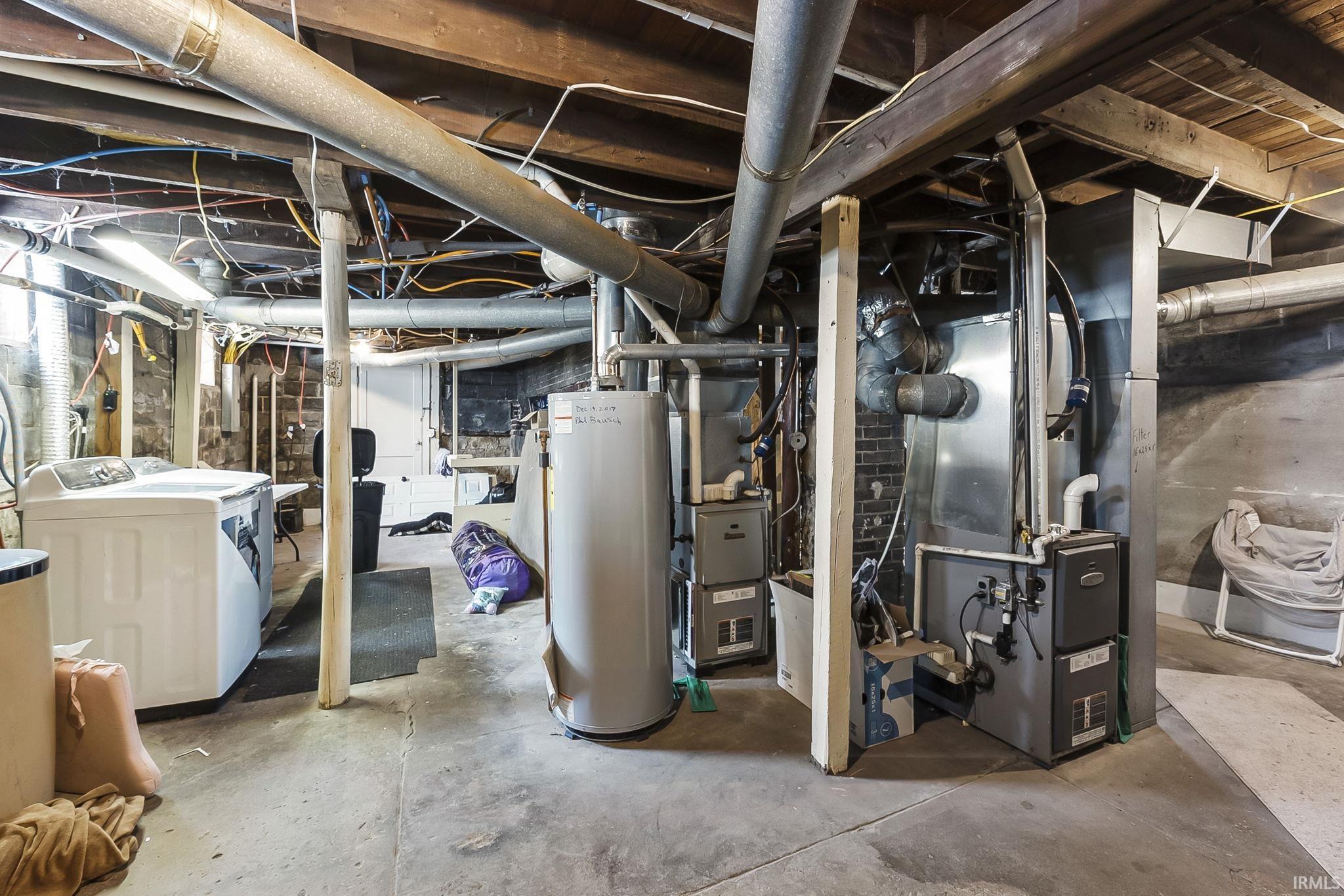Unfinished below grade area featuring gas water heater, heating unit, and washing machine and clothes dryer