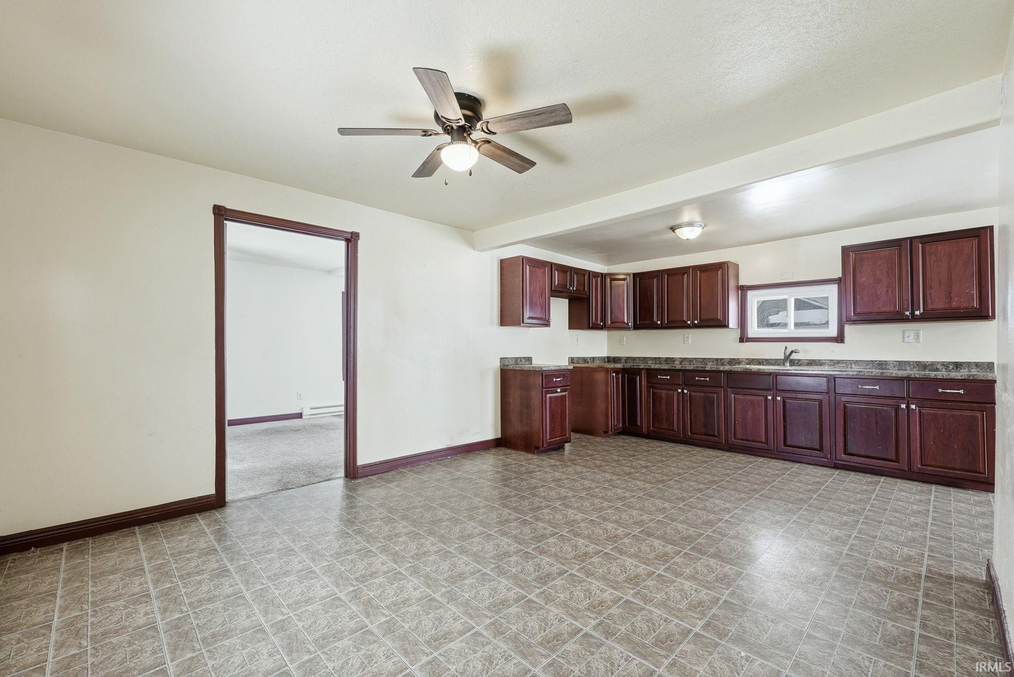 Kitchen with bold wood finish cabinetry, ceiling fan, dark countertops, and a baseboard heating unit