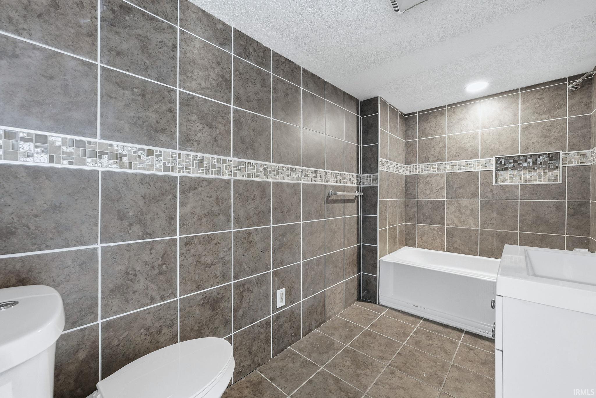 Full bath featuring tile walls, a textured ceiling, vanity, shower / washtub combination, and tile patterned flooring