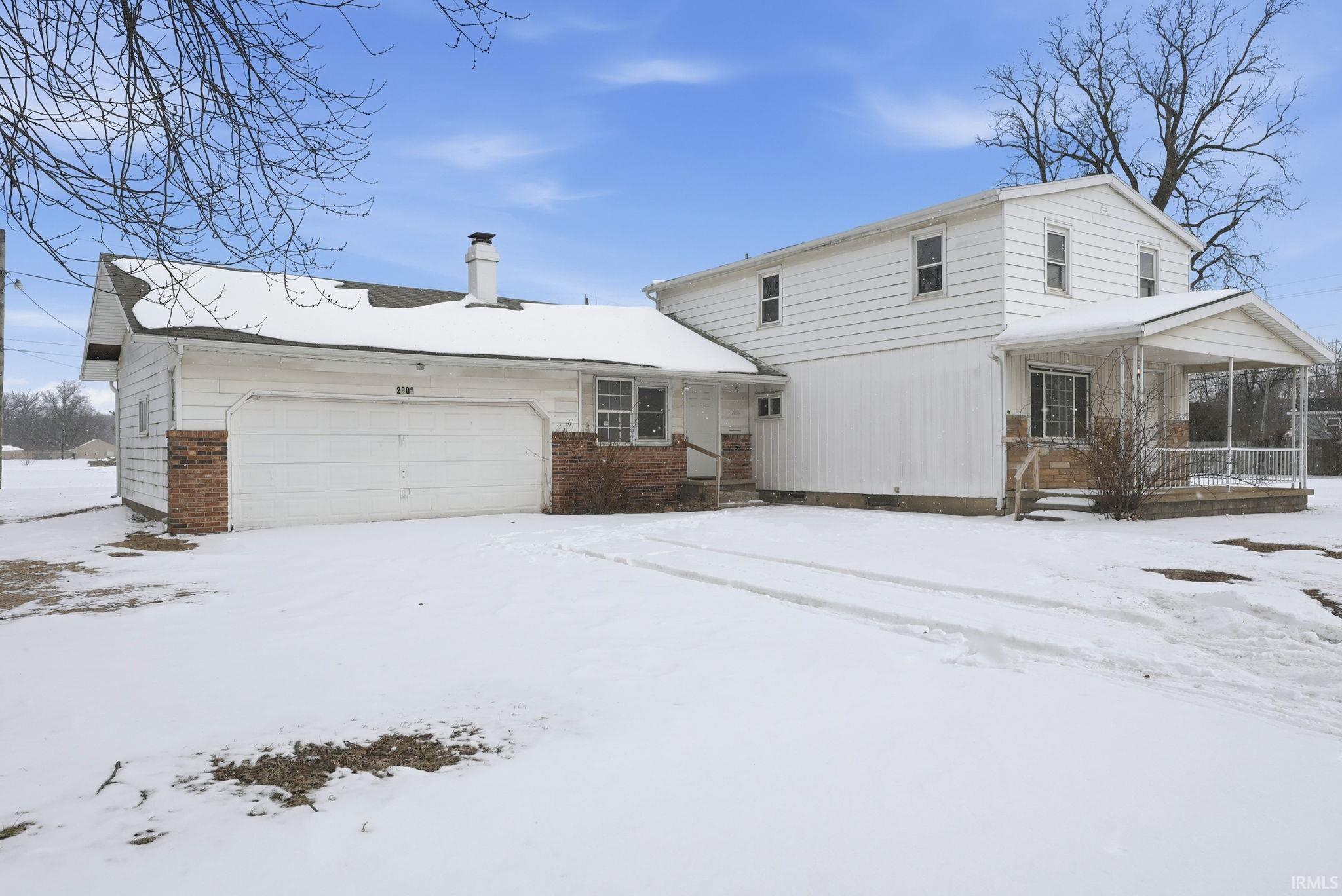 View of front of home featuring a chimney, brick siding, an attached garage, and covered porch