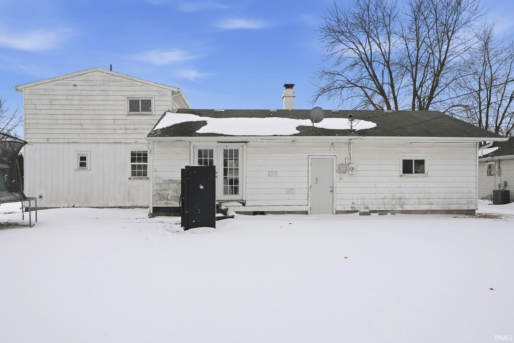 Snow covered house featuring a trampoline, a chimney, and french doors