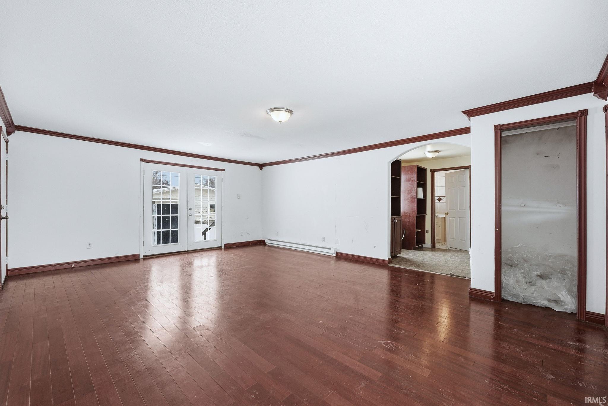 Empty room featuring arched walkways, dark wood finished floors, baseboard heating, and crown molding