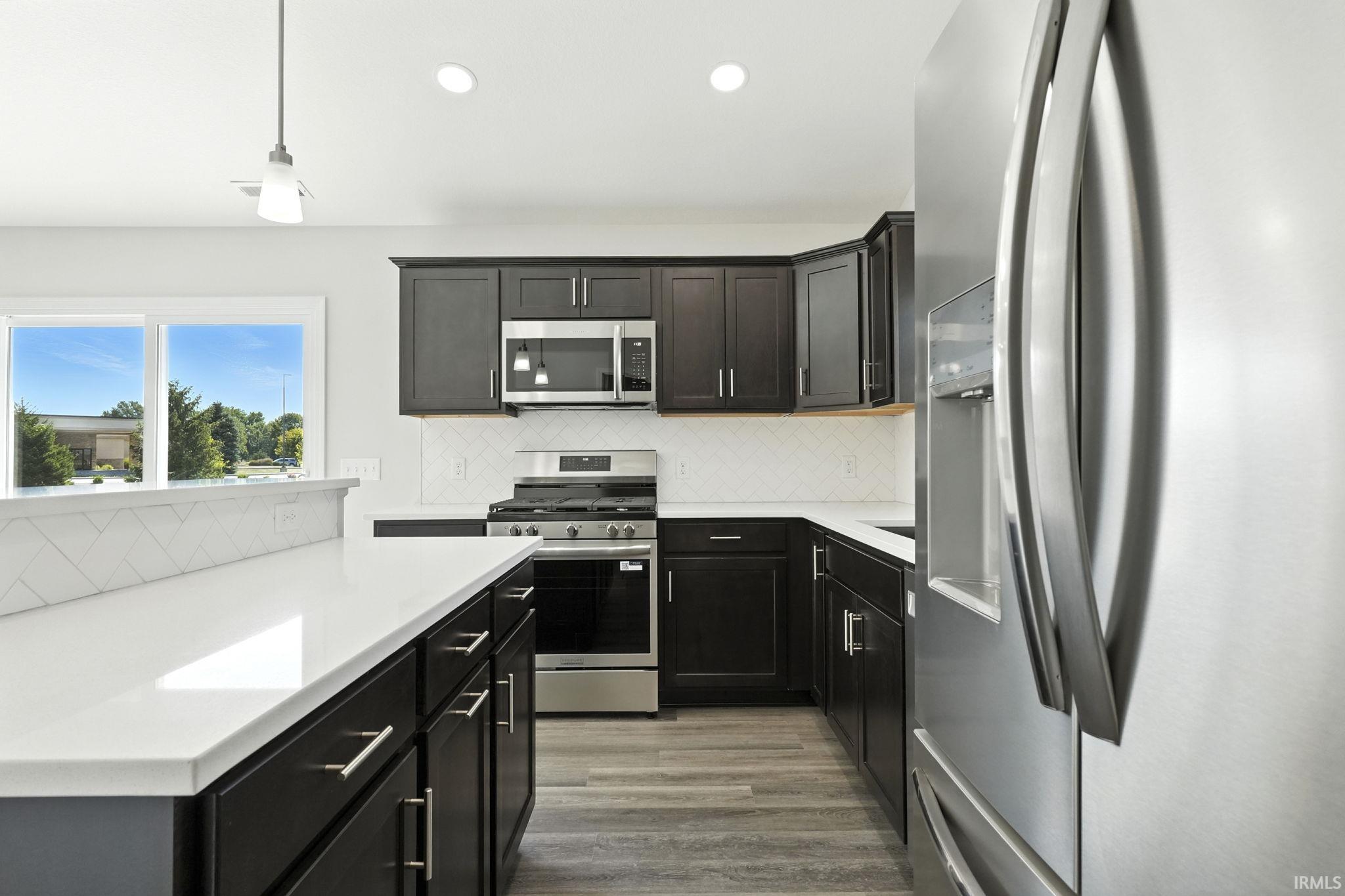 Kitchen featuring stainless steel appliances, decorative light fixtures, light wood finished floors, tasteful backsplash, and light stone counters