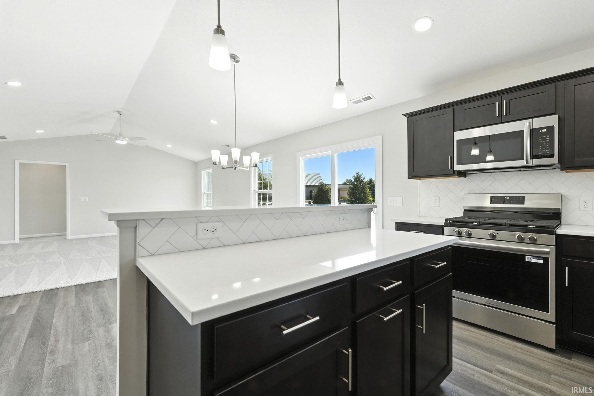 Kitchen featuring dark cabinetry, stainless steel appliances, light wood finished floors, tasteful backsplash, and light stone counters