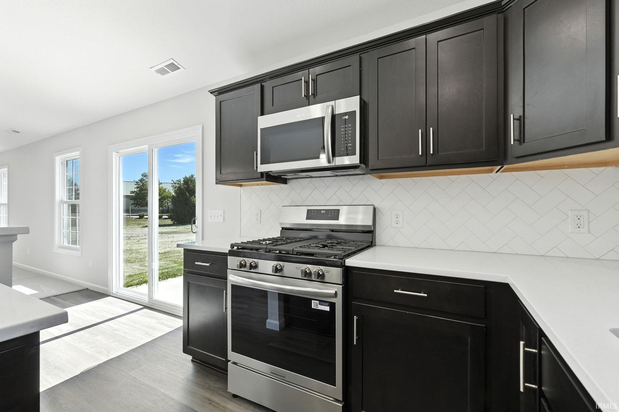 Kitchen featuring stainless steel appliances, dark wood-style floors, dark cabinetry, and light stone counters