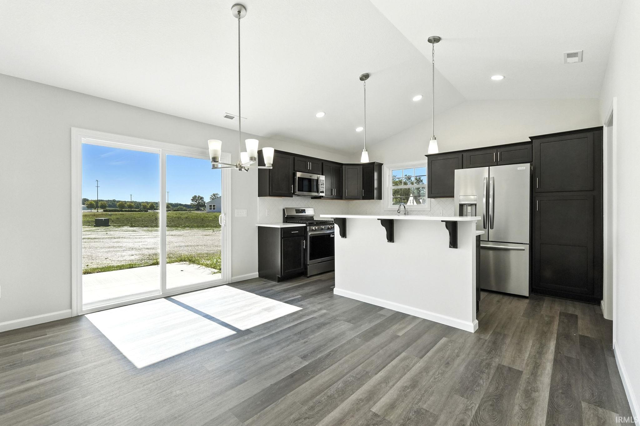 Kitchen featuring stainless steel appliances, vaulted ceiling, a kitchen bar, suspended lighting, and dark cabinets