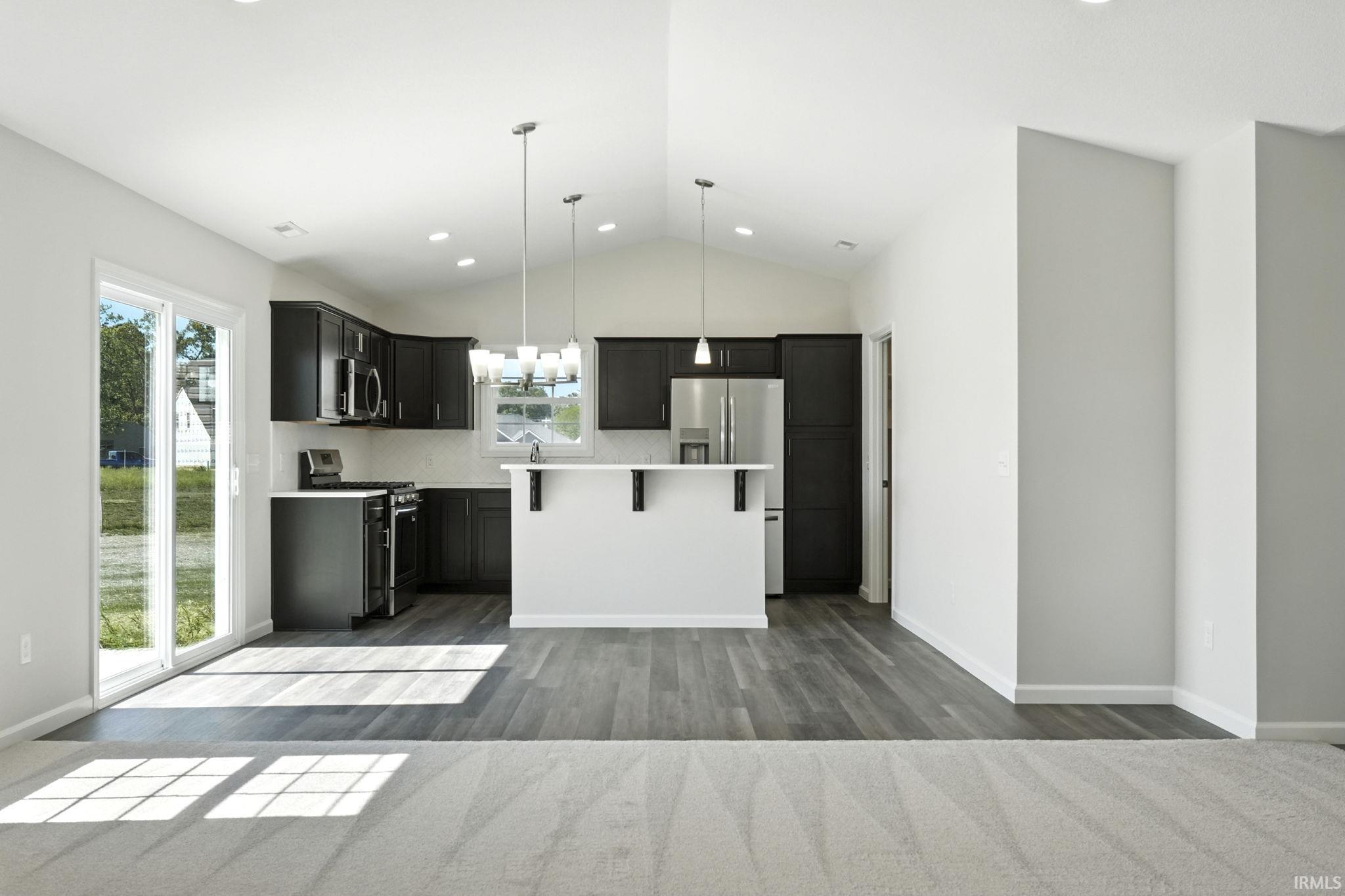 Kitchen with light countertops, stainless steel appliances, a kitchen island, dark cabinetry, and suspended lighting
