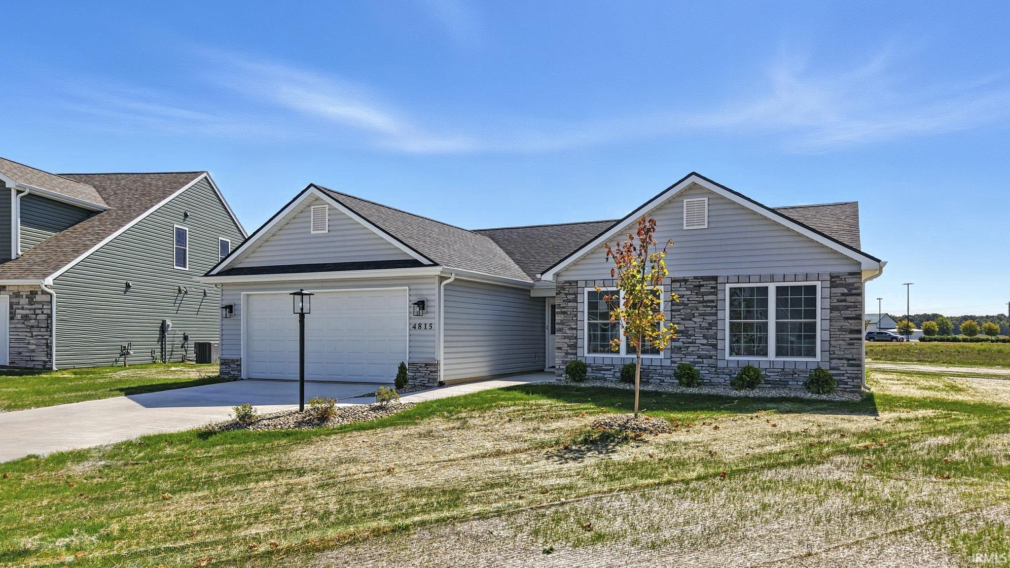 View of front of home with concrete driveway, stone siding, a front lawn, a garage, and a shingled roof