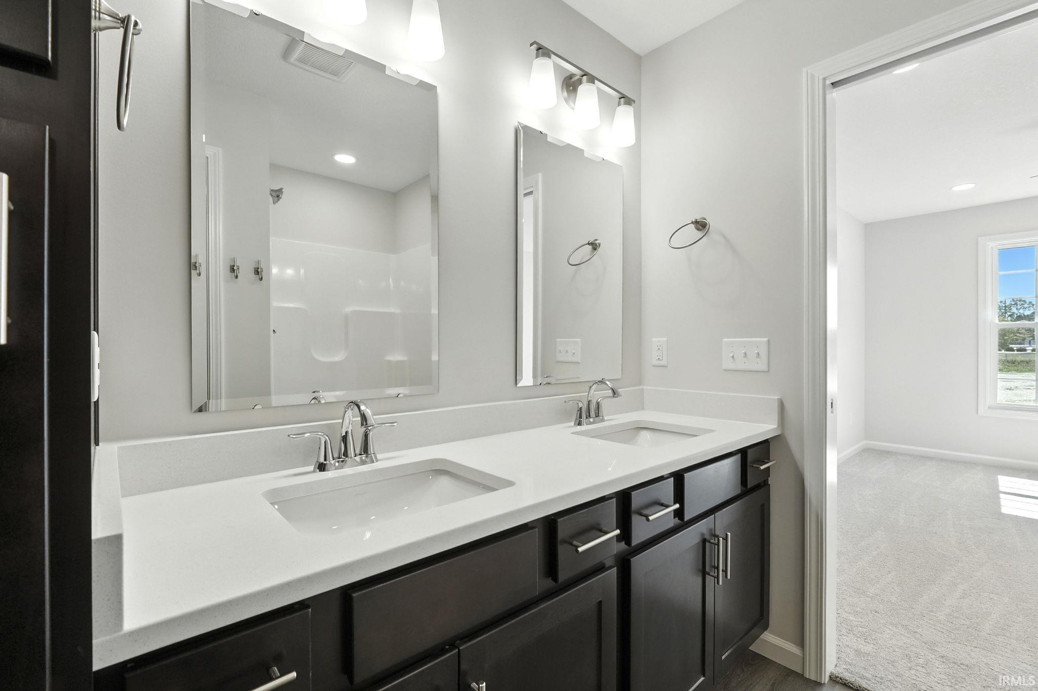 Bathroom with double vanity, a shower, and dark carpet