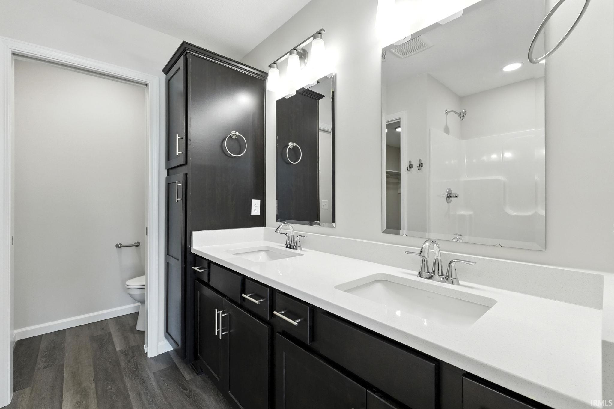 Bathroom featuring double vanity, a shower, and dark wood finished floors