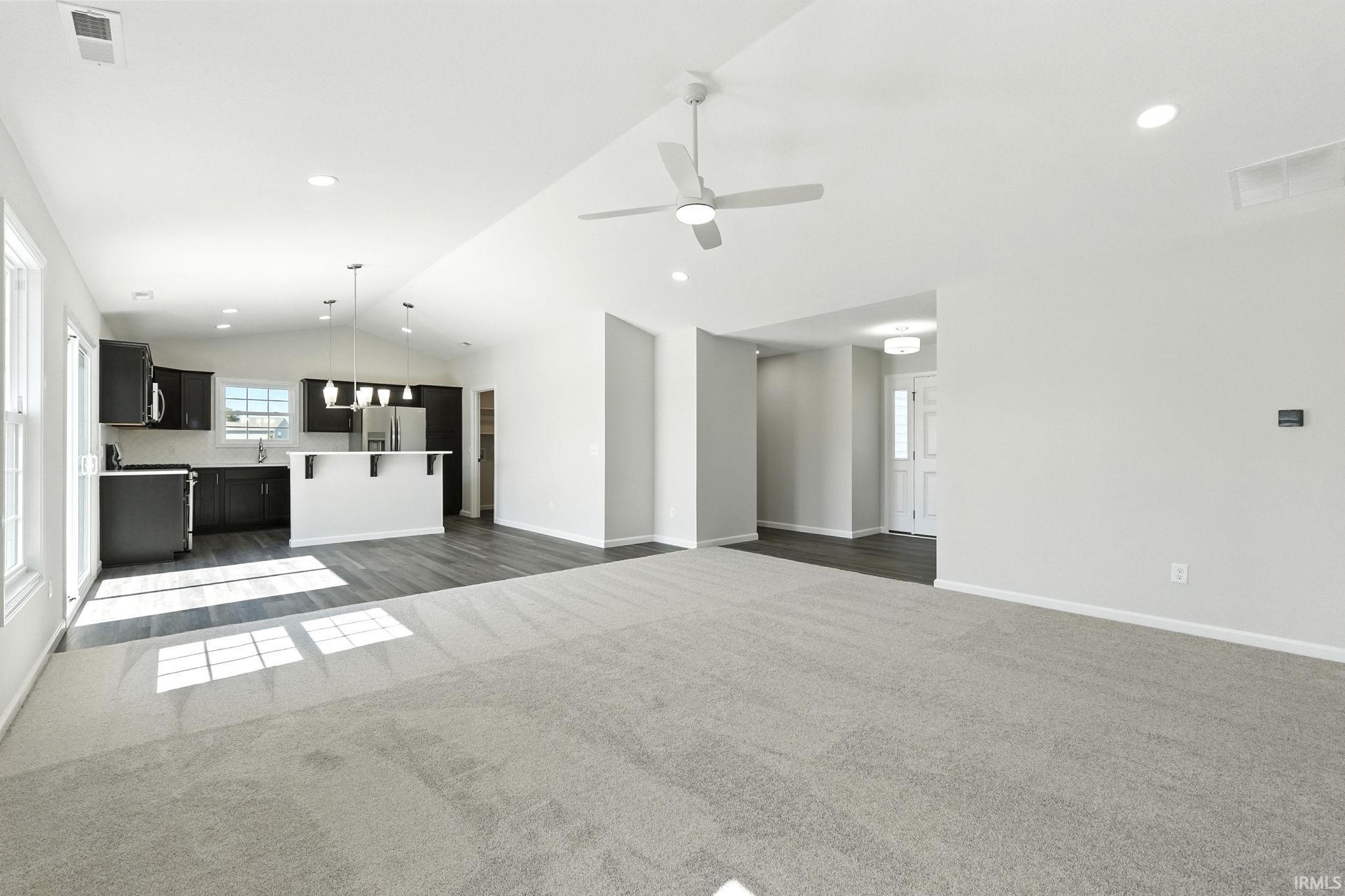 Unfurnished living room featuring vaulted ceiling, dark colored carpet, a ceiling fan, and recessed lighting