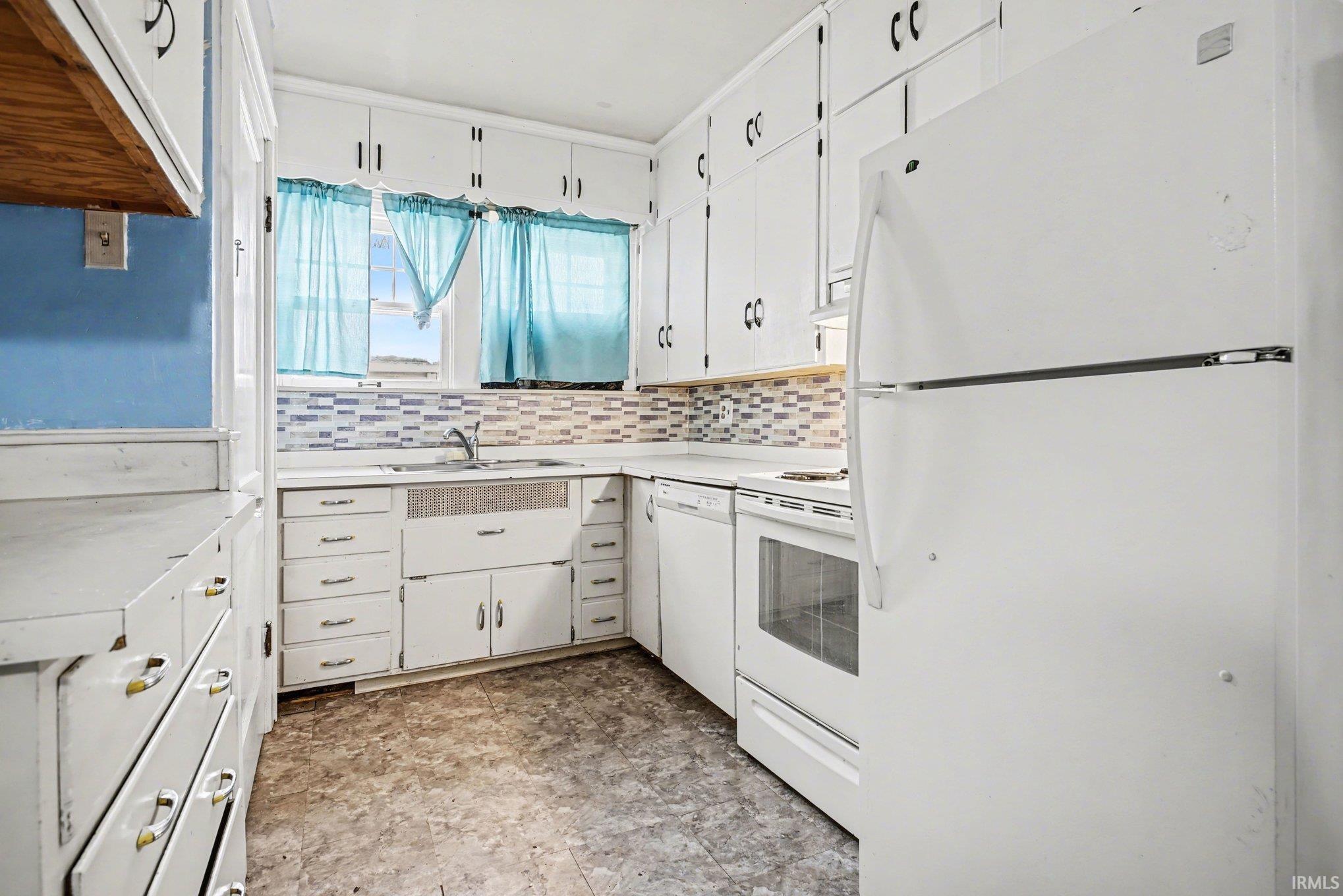 Kitchen with white appliances, white cabinets, light countertops, and tasteful backsplash
