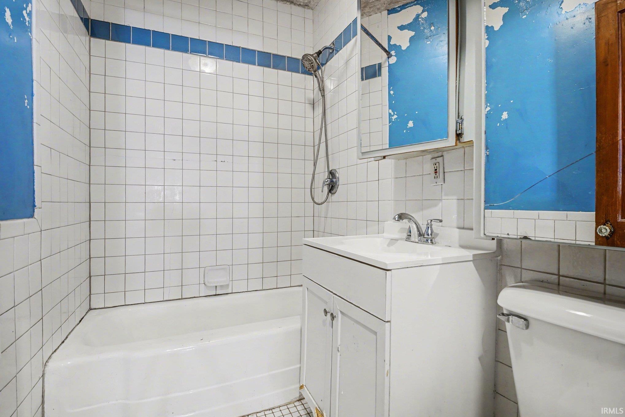 Full bath with tile walls, bathtub / shower combination, vanity, and backsplash