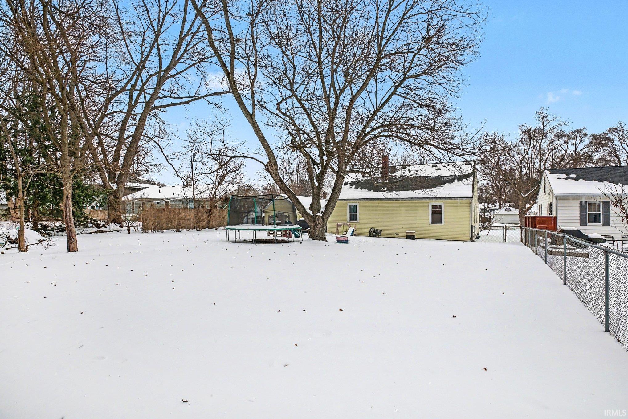 Snowy yard with a fenced backyard, a trampoline, and a wooden deck