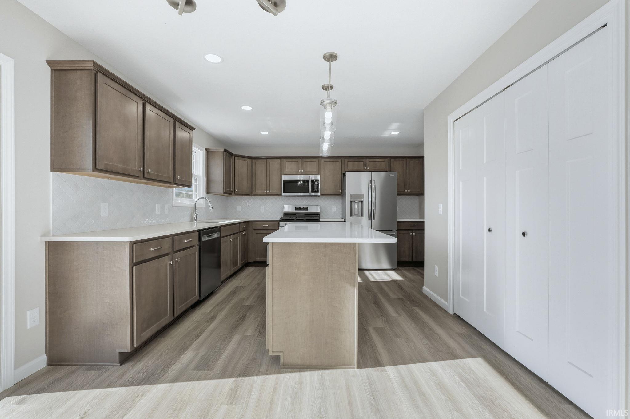 Kitchen featuring stainless steel appliances, pendant lighting, light wood finished floors, and a kitchen island