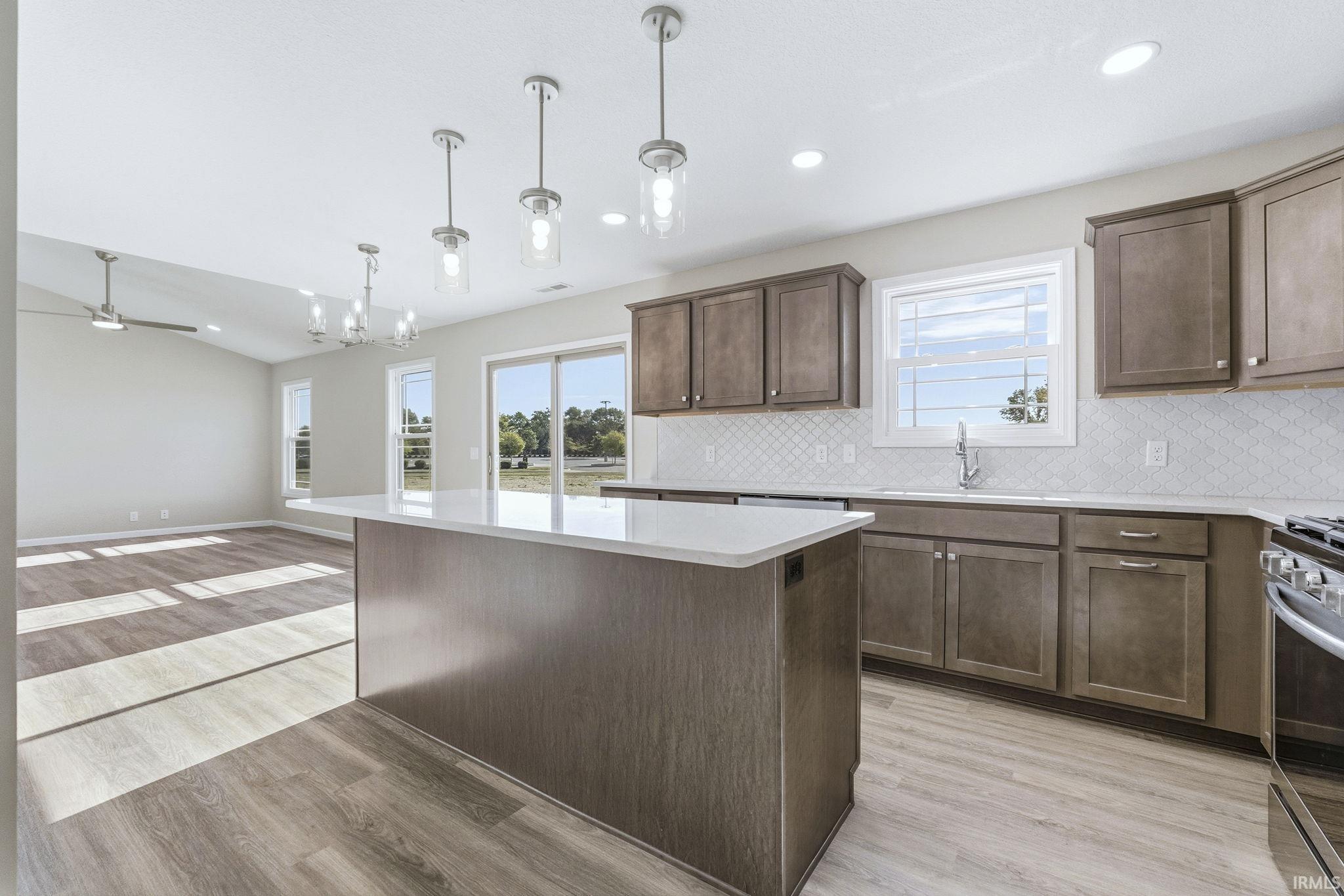 Kitchen with light wood-style floors, dark wood finish cabinets, open floor plan, a center island, and lofted ceiling
