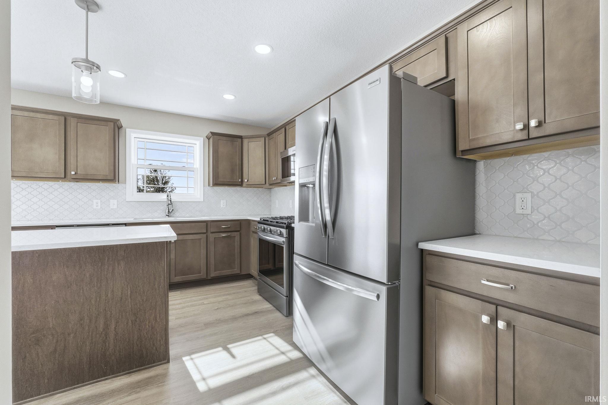 Kitchen featuring hanging light fixtures, stainless steel appliances, light wood finished floors, backsplash, and light stone counters