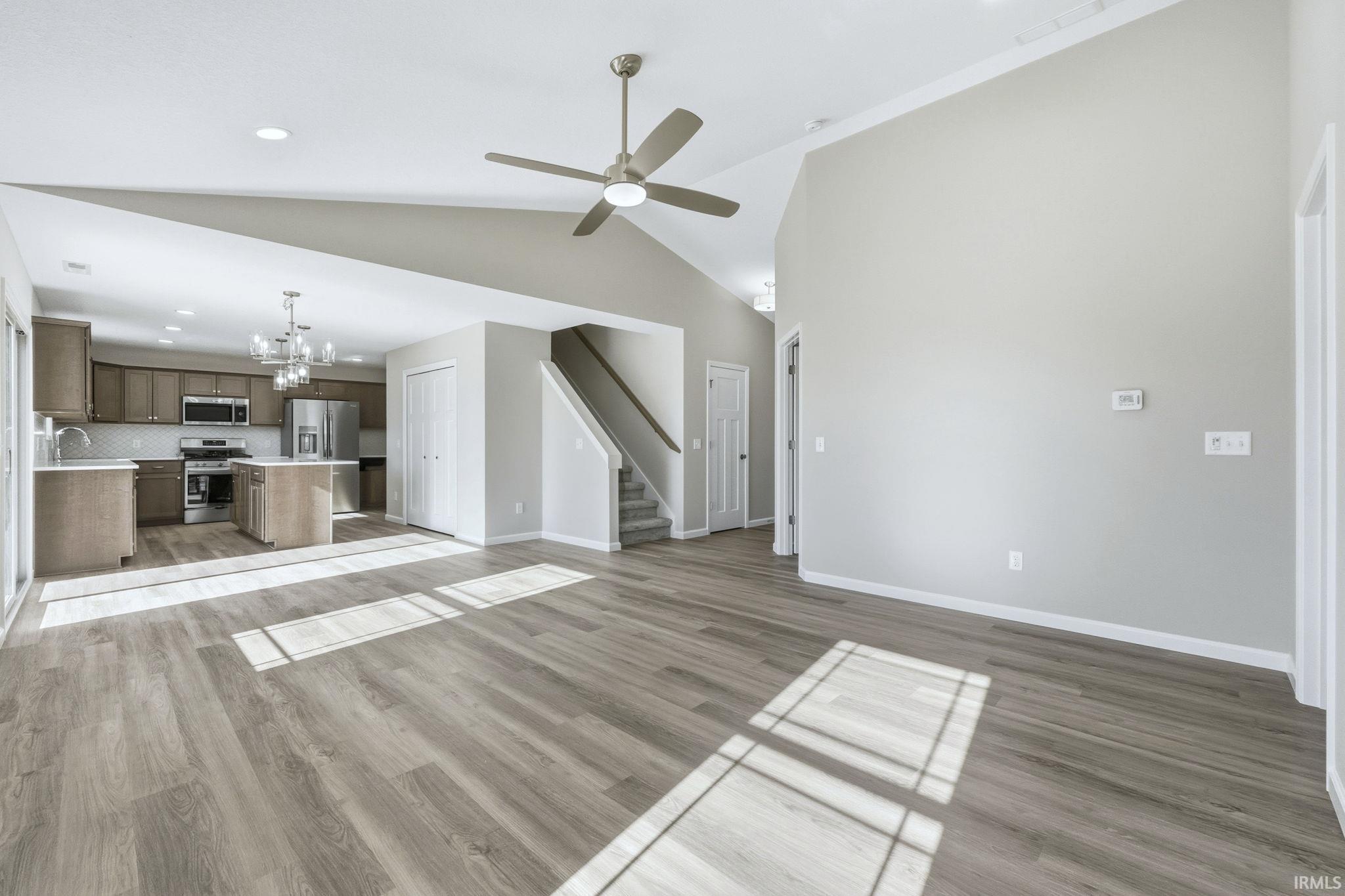 Unfurnished living room with a chandelier, lofted ceiling, a ceiling fan, and light wood-style flooring