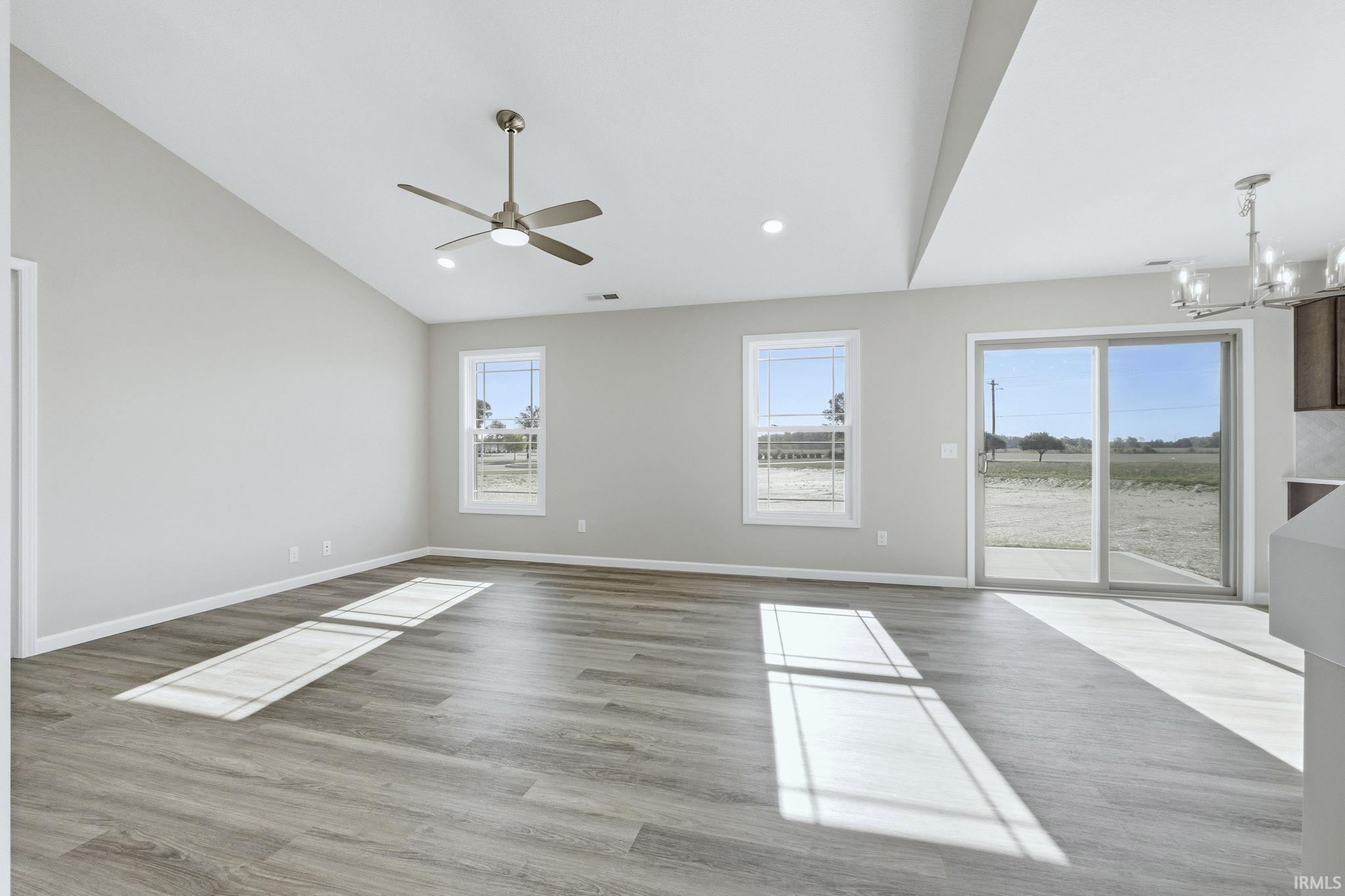 Empty room featuring vaulted ceiling, suspended lighting, light wood-style flooring, and ceiling fan