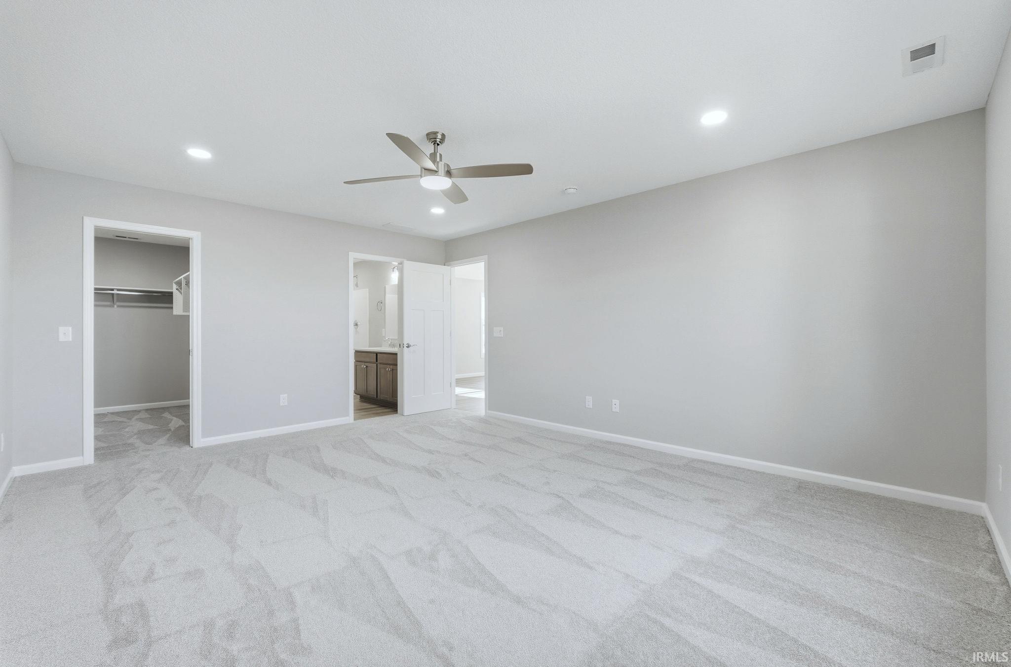 Unfurnished bedroom featuring a walk in closet, light colored carpet, ensuite bath, recessed lighting, and ceiling fan