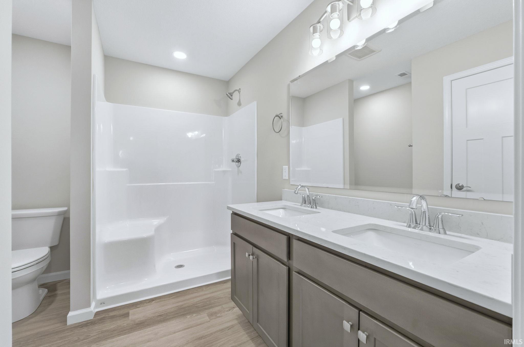Bathroom with double vanity, a stall shower, light wood-type flooring, and recessed lighting