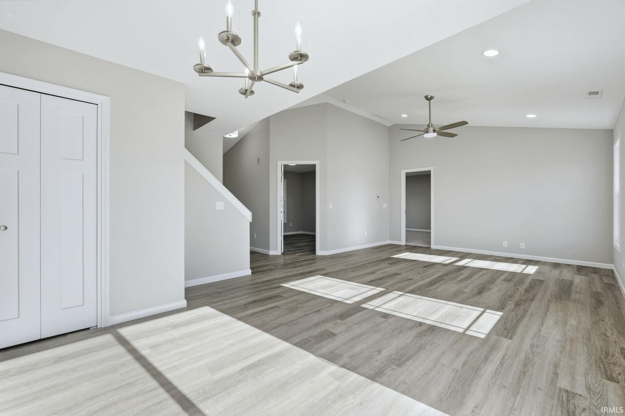 Unfurnished living room with a chandelier, light wood-style flooring, lofted ceiling, and a ceiling fan