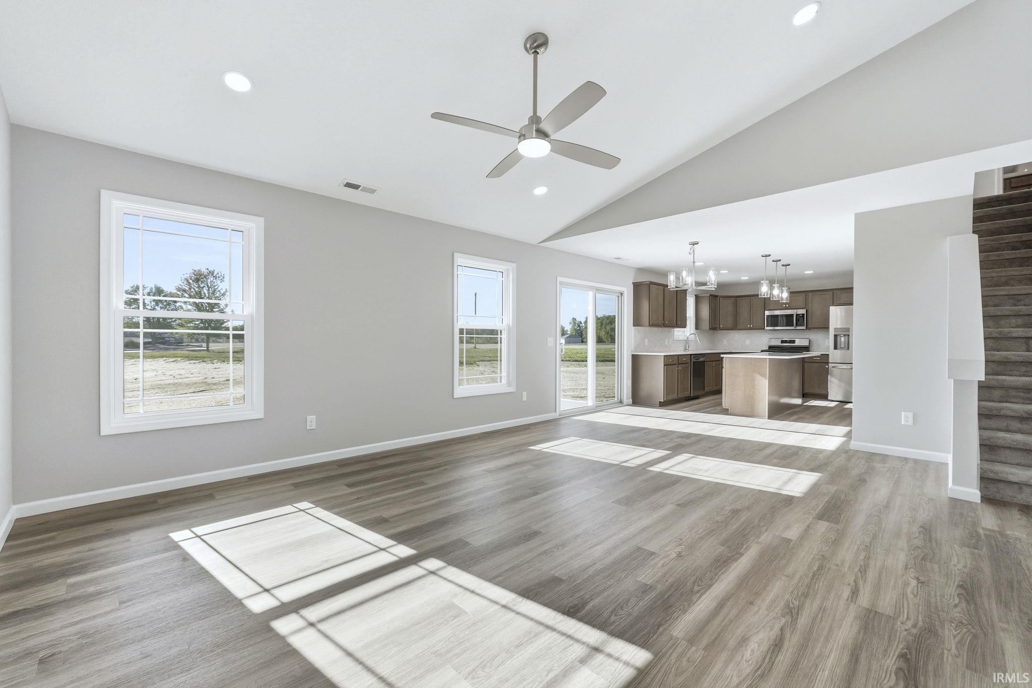 Unfurnished living room with ceiling fan, vaulted ceiling, light wood-style flooring, and a chandelier