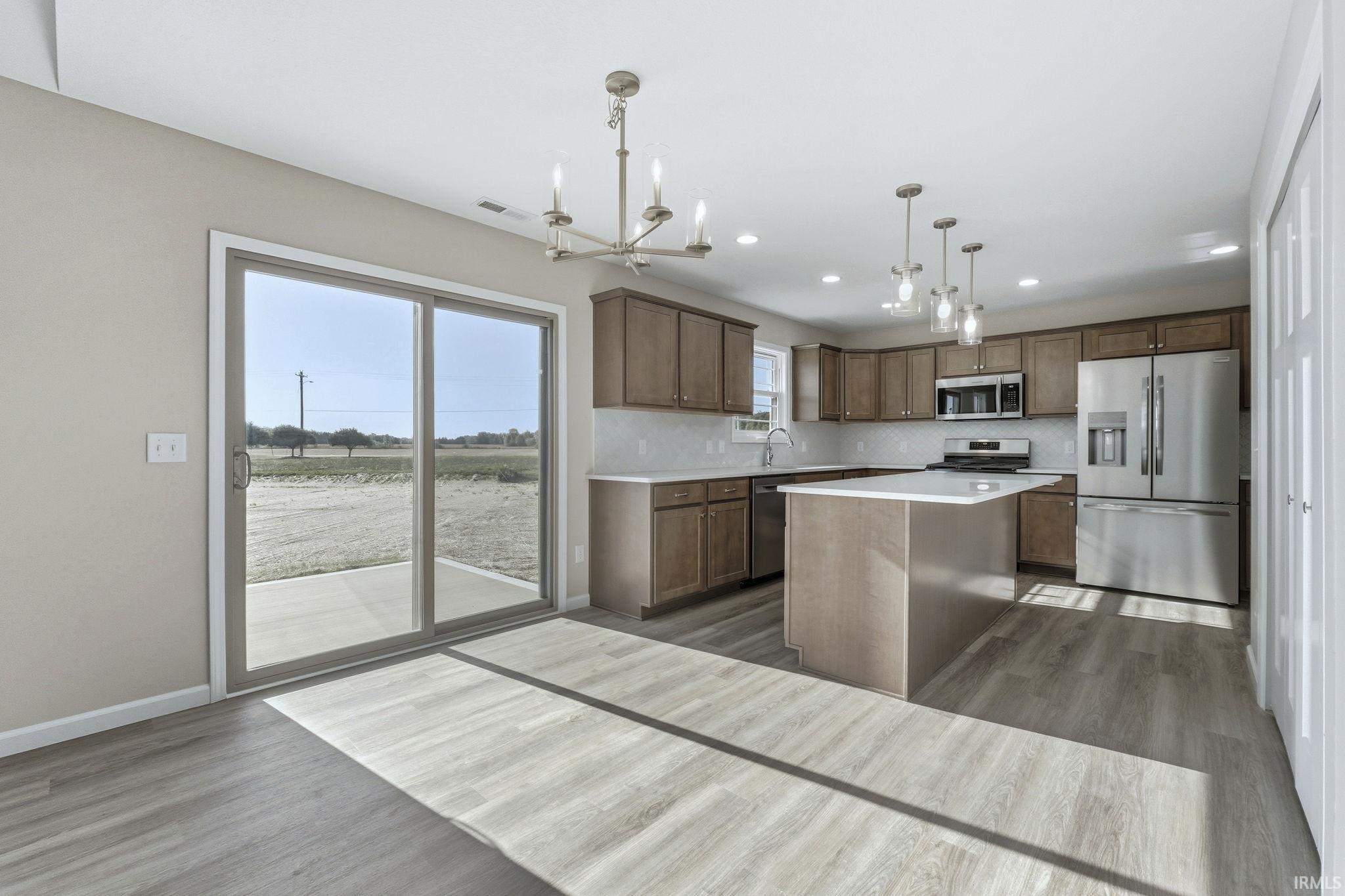 Kitchen with stainless steel appliances, dark wood finished floors, a kitchen island, a chandelier, and decorative backsplash