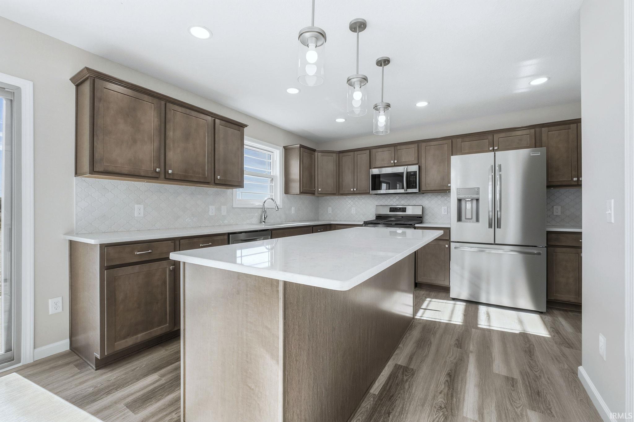 Kitchen with stainless steel appliances, pendant lighting, dark wood finish cabinets, light wood-style floors, and a center island
