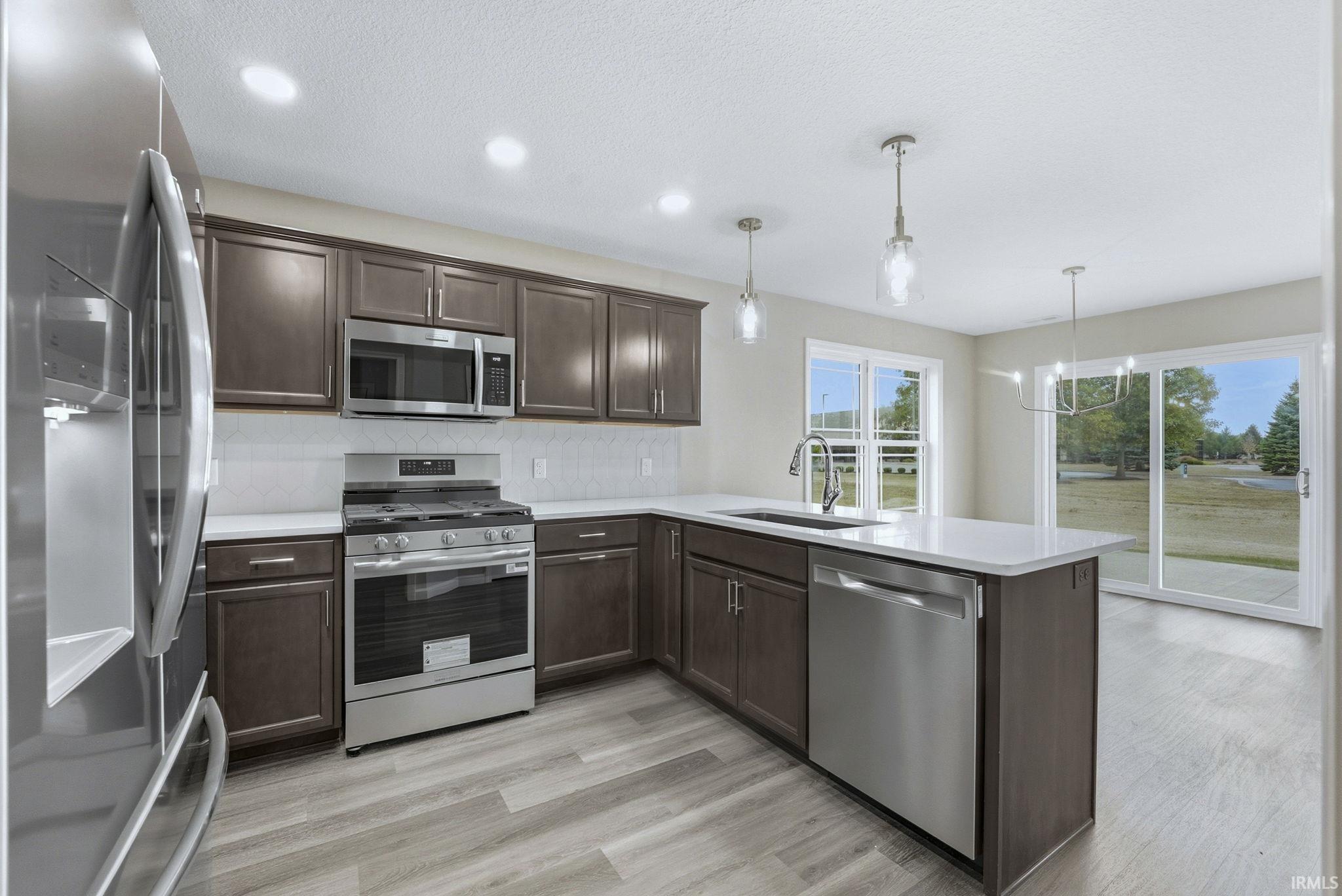 Kitchen featuring stainless steel appliances, dark wood finish cabinetry, a peninsula, light wood finished floors, and decorative backsplash