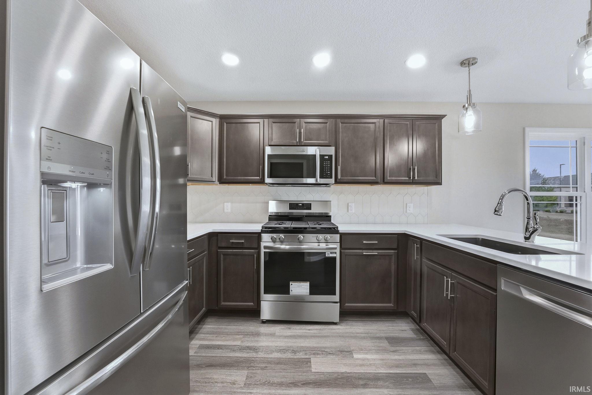 Kitchen featuring stainless steel appliances, dark wood finish cabinetry, pendant lighting, backsplash, and light wood-type flooring