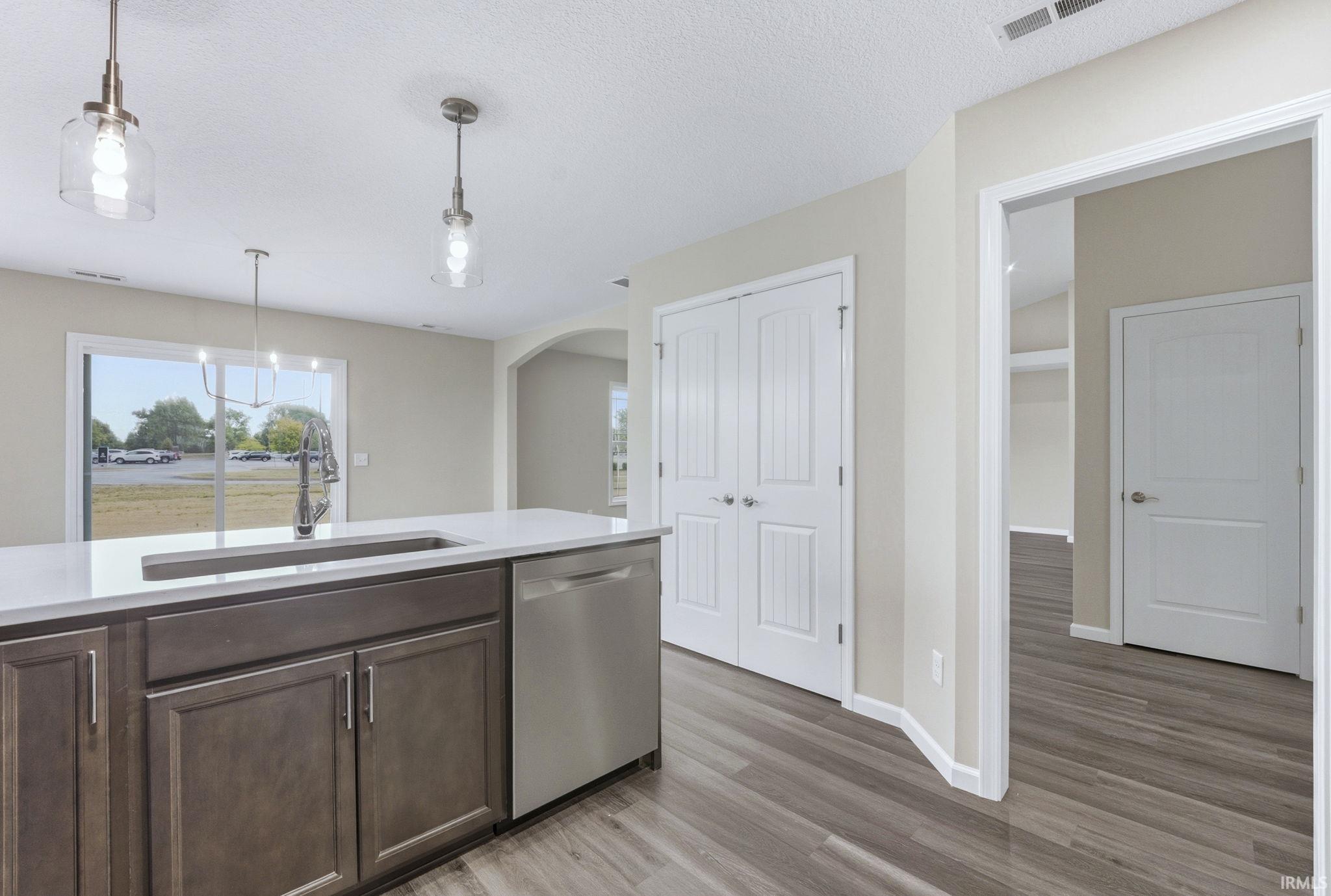 Kitchen with dark wood finish cabinets, dishwasher, light wood finished floors, arched walkways, and hanging light fixtures