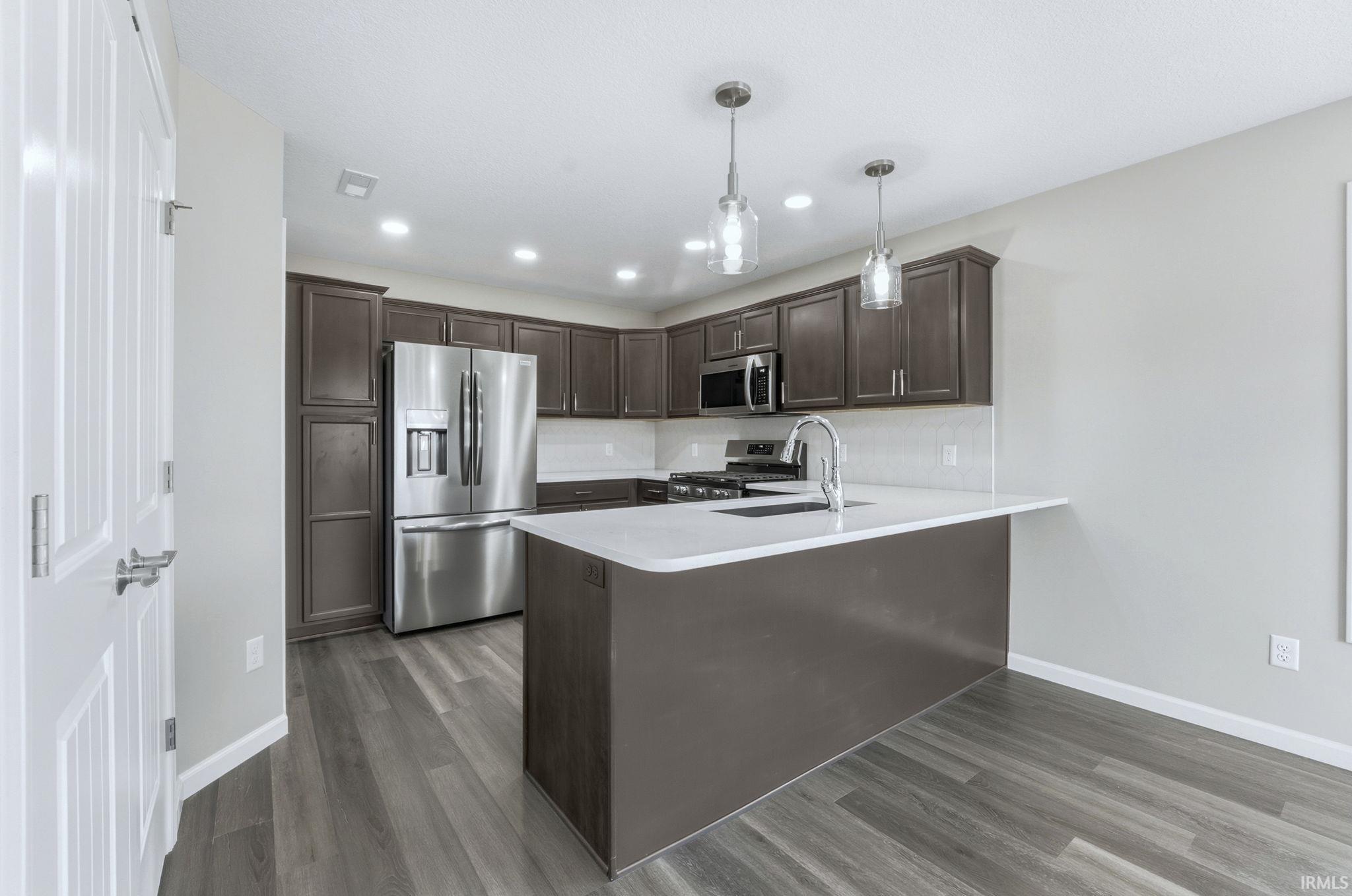 Kitchen featuring dark wood finish cabinetry, stainless steel appliances, a peninsula, and dark wood-style flooring