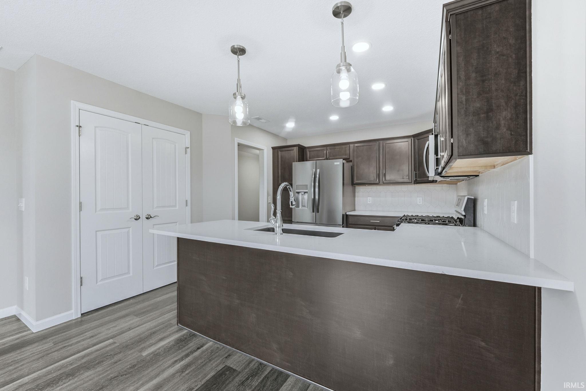 Kitchen with dark wood finish cabinetry, a peninsula, stainless steel appliances, pendant lighting, and decorative backsplash