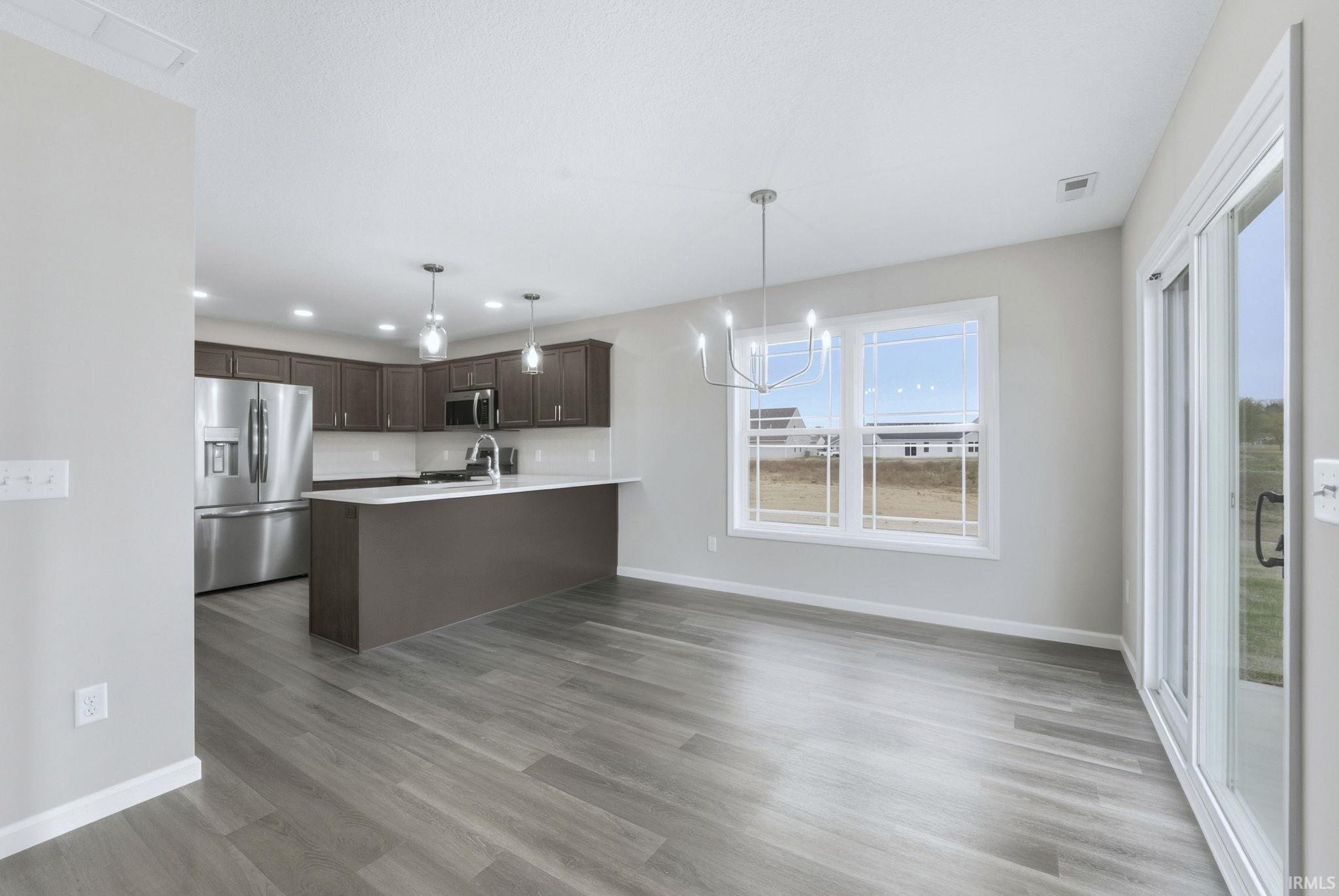 Kitchen featuring hanging lights, dark wood finish cabinets, stainless steel appliances, a peninsula, and light wood-style floors