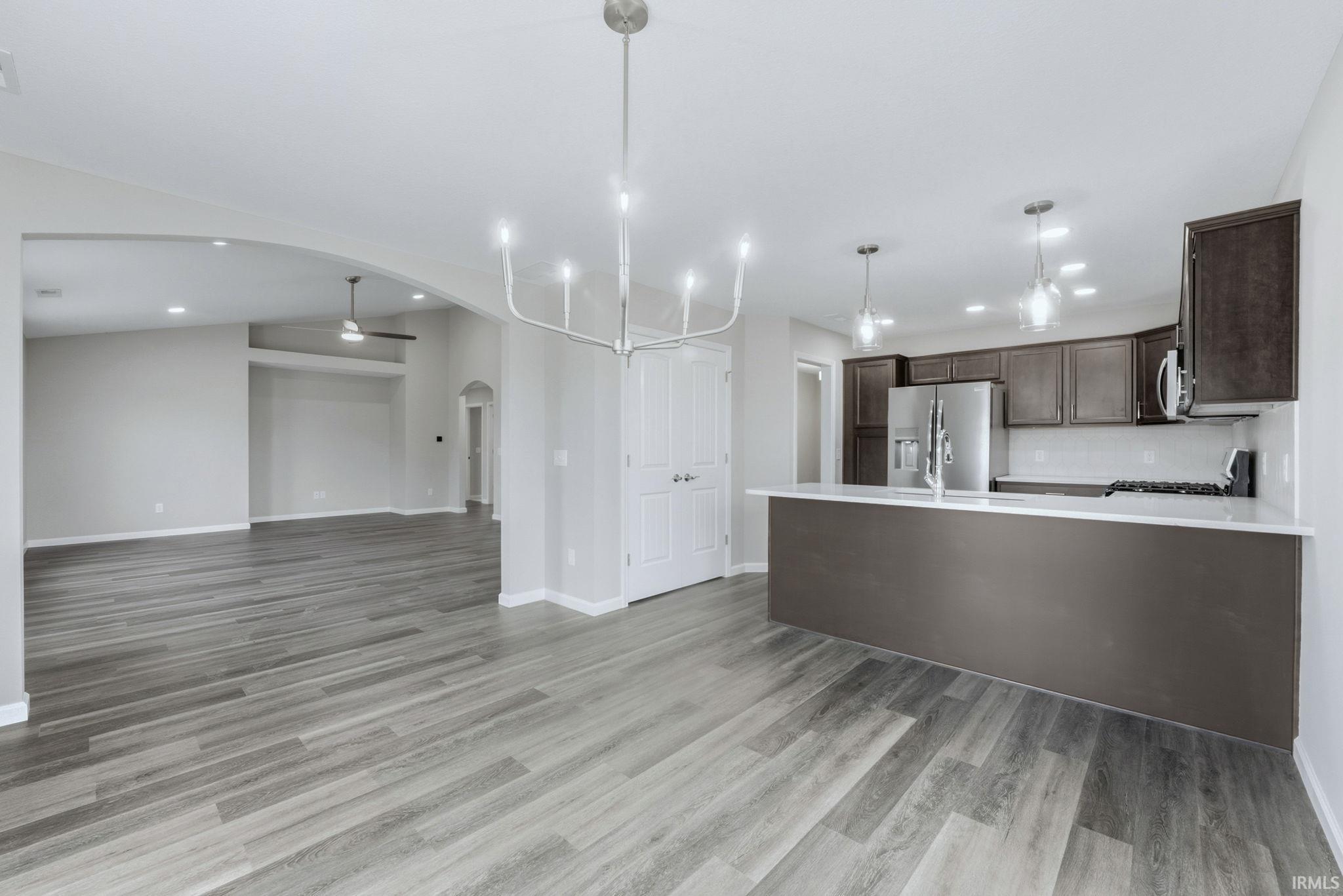 Kitchen with dark wood finish cabinets, a peninsula, open floor plan, stainless steel fridge, and arched walkways