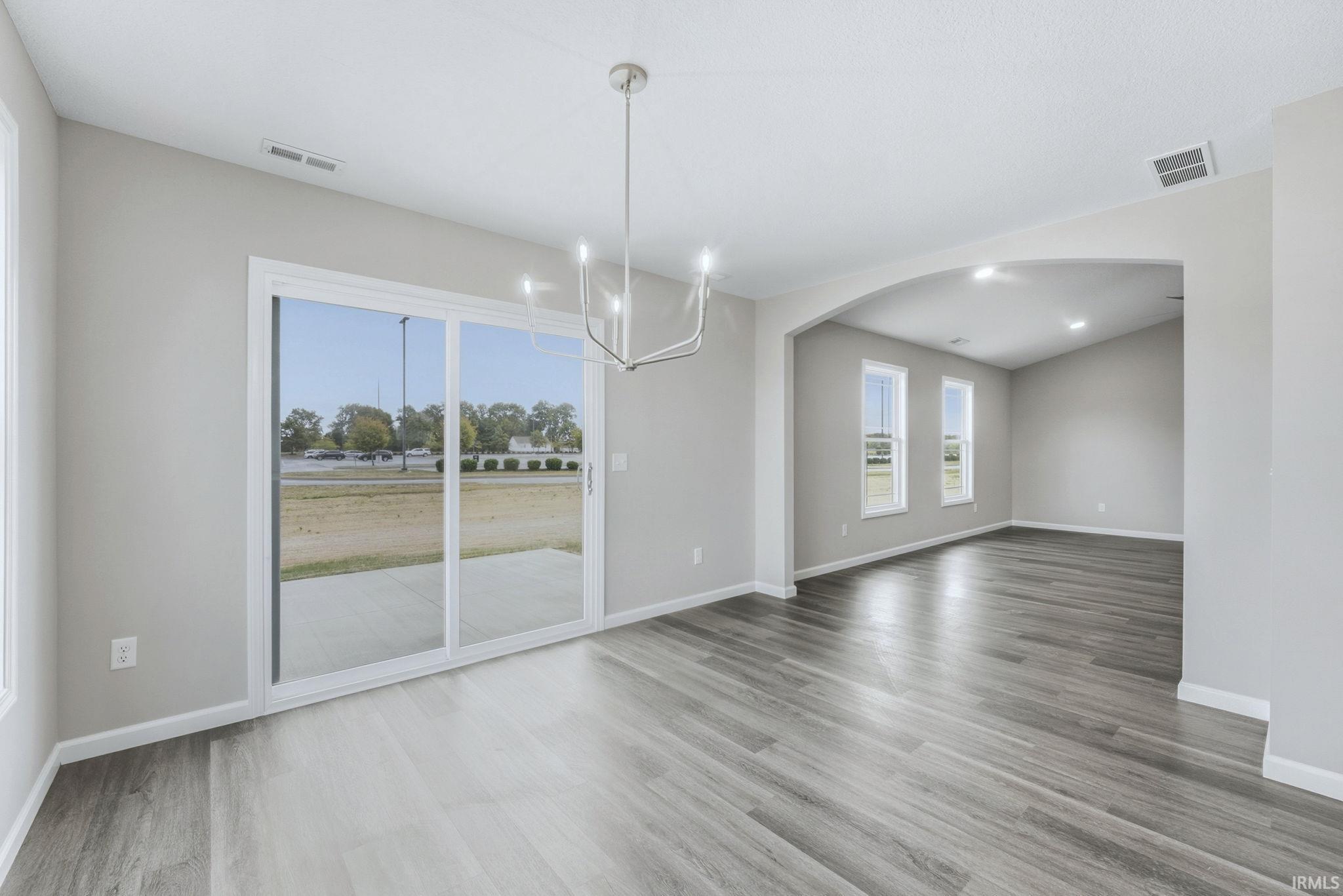 Unfurnished dining area with suspended lighting, arched walkways, and light wood-style flooring