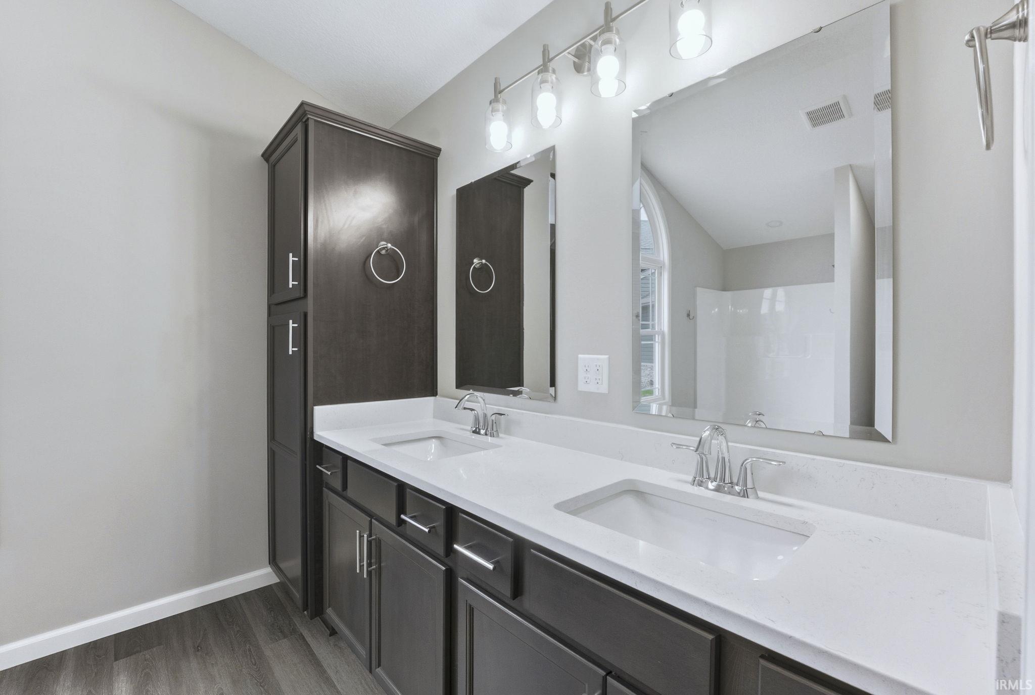 Full bathroom with double vanity, dark wood-style flooring, and a shower
