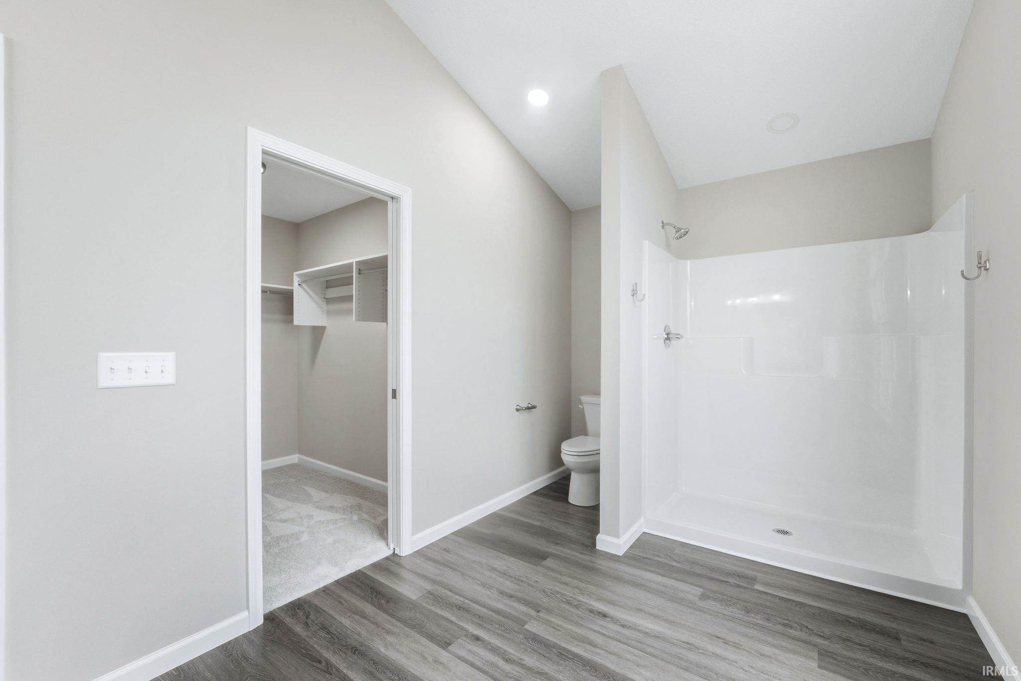 Full bath featuring a spacious closet, a shower stall, and light wood-style floors