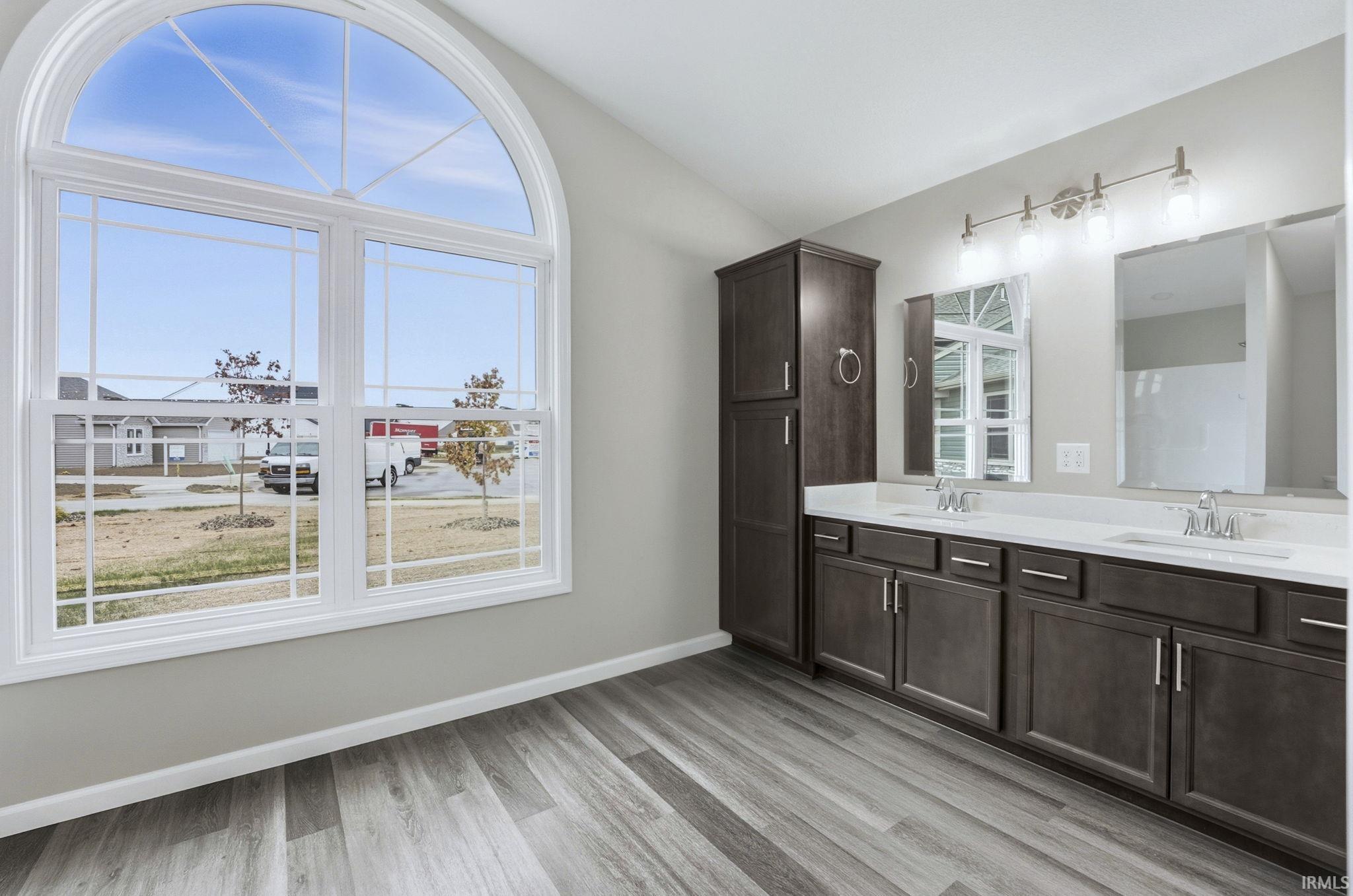 Bathroom with double vanity, light wood-type flooring, and vaulted ceiling