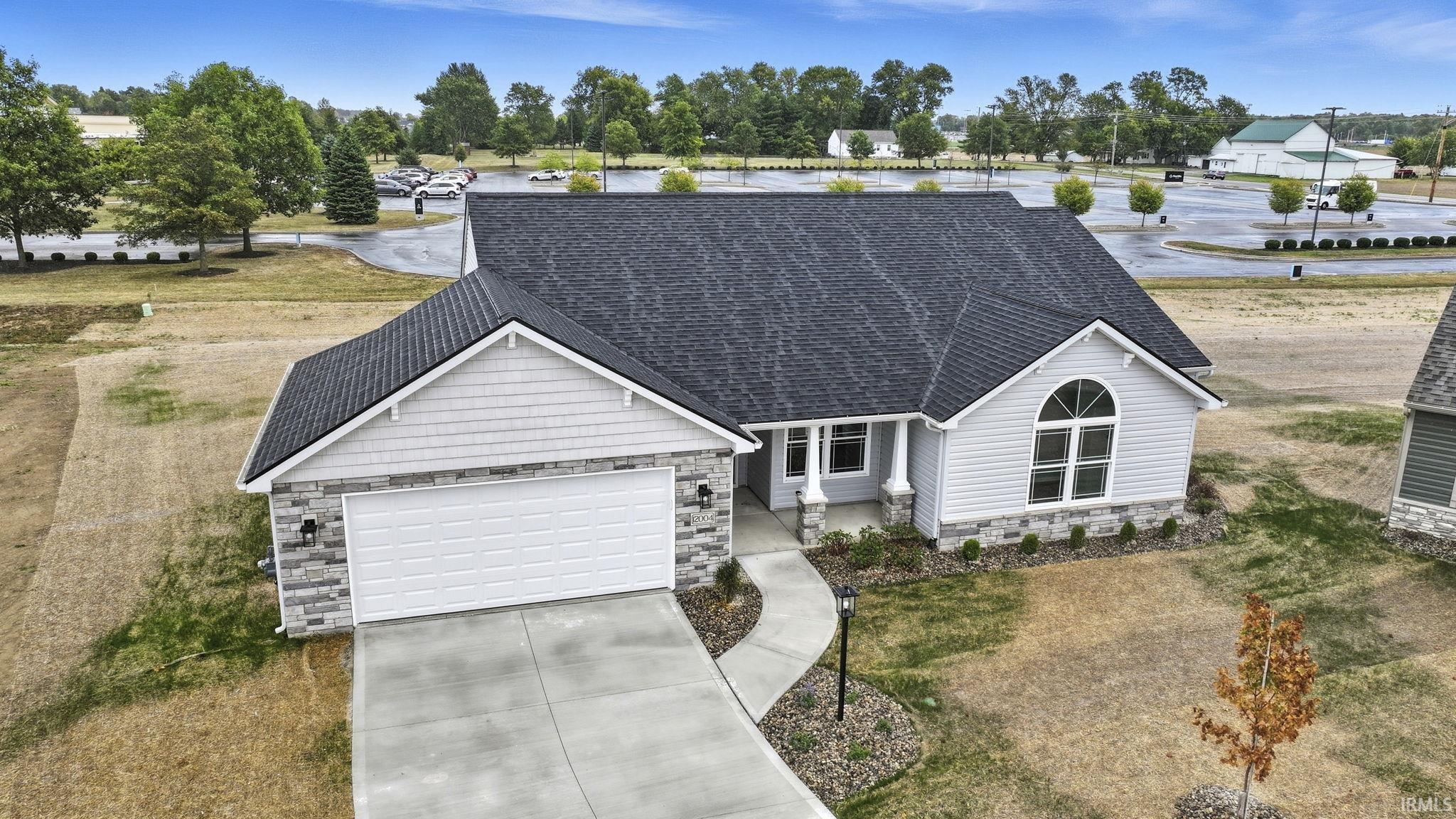 View of front of home with stone siding, a shingled roof, concrete driveway, a garage, and a front lawn