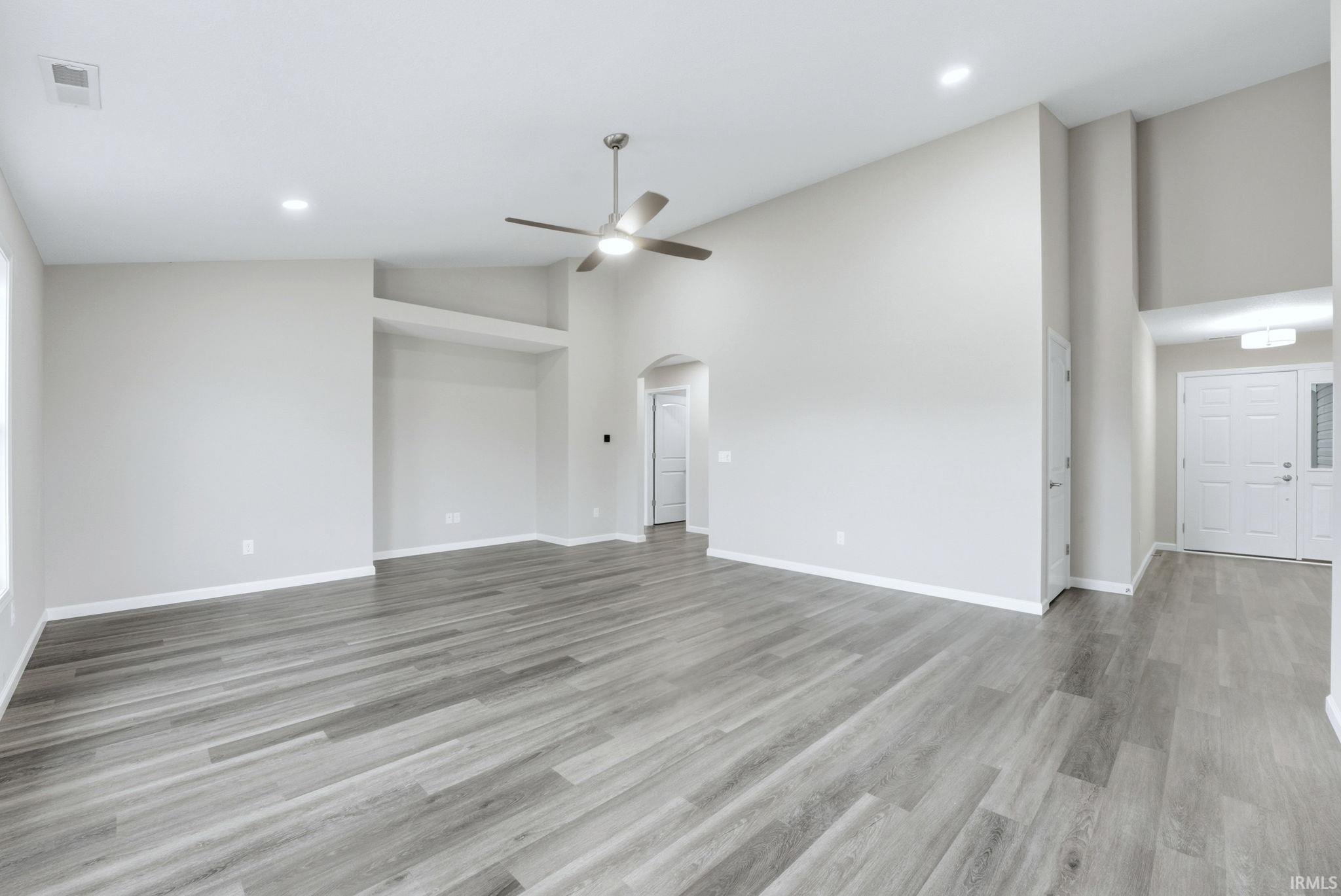 Unfurnished living room with arched walkways, a ceiling fan, lofted ceiling, light wood-style floors, and recessed lighting