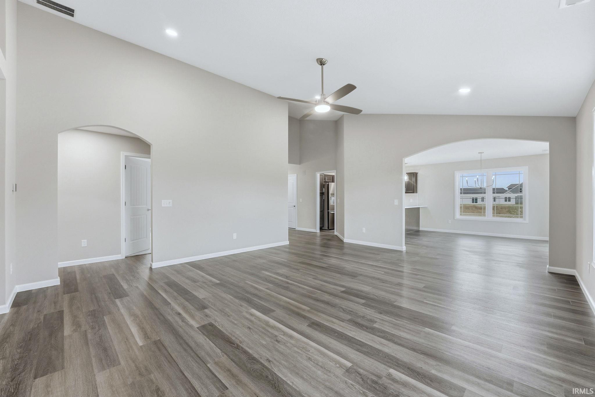 Unfurnished living room with arched walkways, ceiling fan, light wood-type flooring, recessed lighting, and a high ceiling